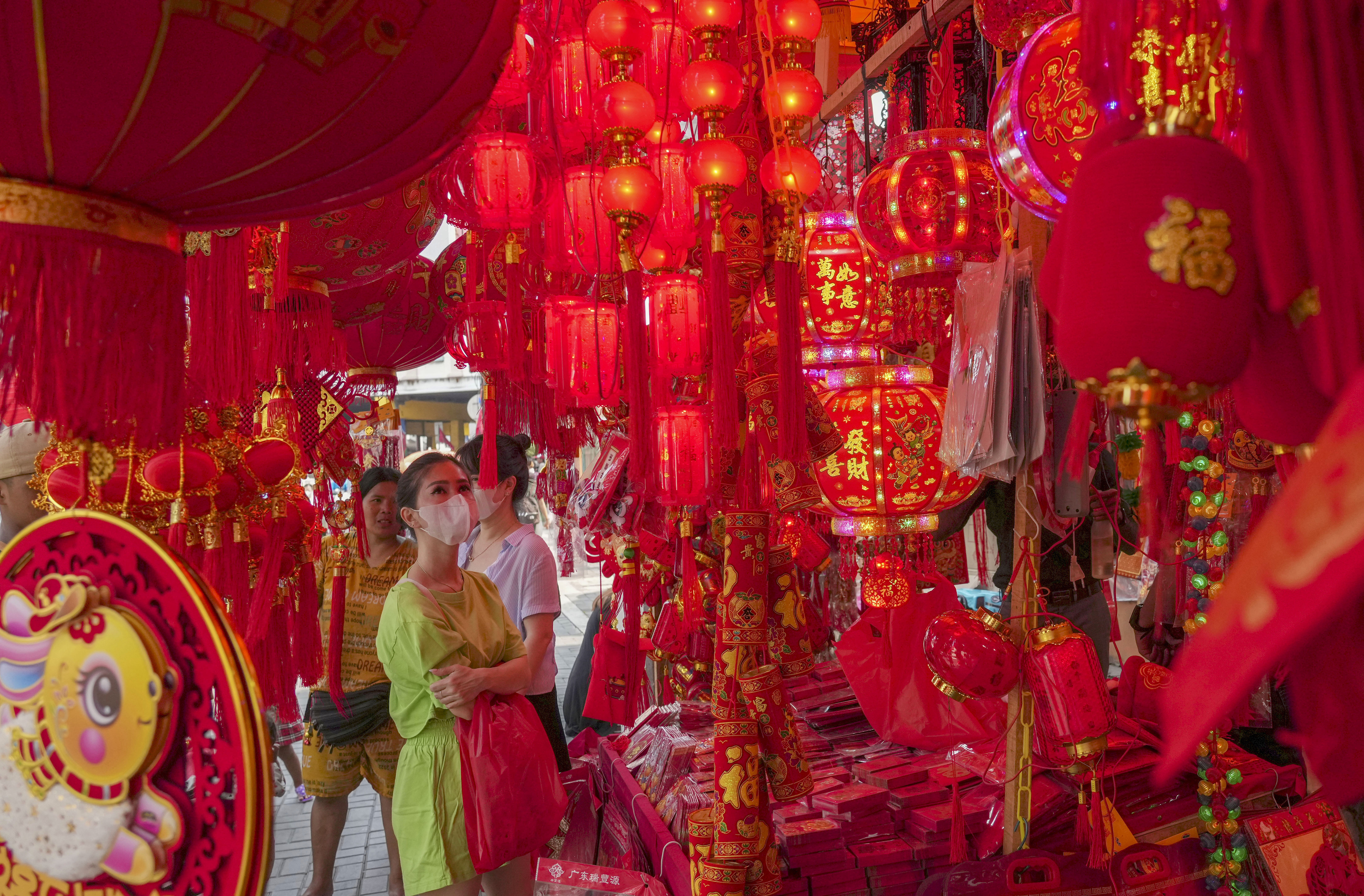 A woman shopping for Lunar New Year decorations in Jakarta's Chinatown. She is in line green and the stalls around her are decked out in red lanterns