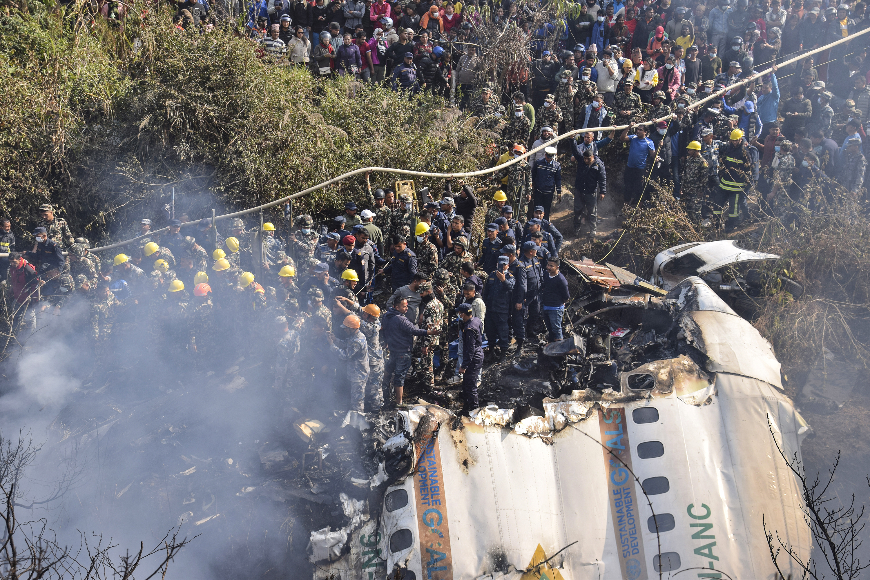 Nepalese rescue workers and civilians gather around the wreckage of a passenger plane that crashed in Pokhara, Nepal
