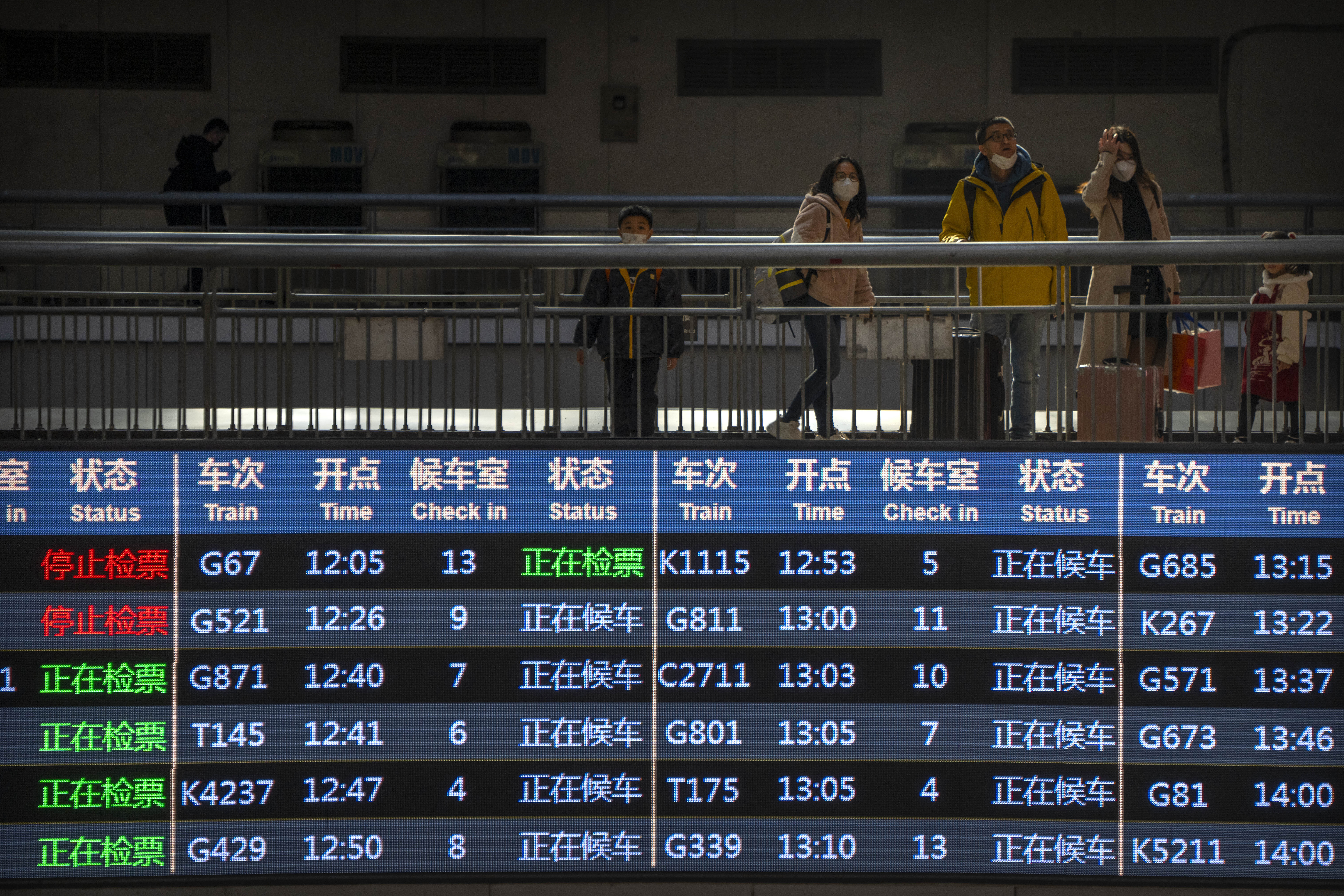 Travelers stand on an elevated walkway near an electronic schedule display at Beijing