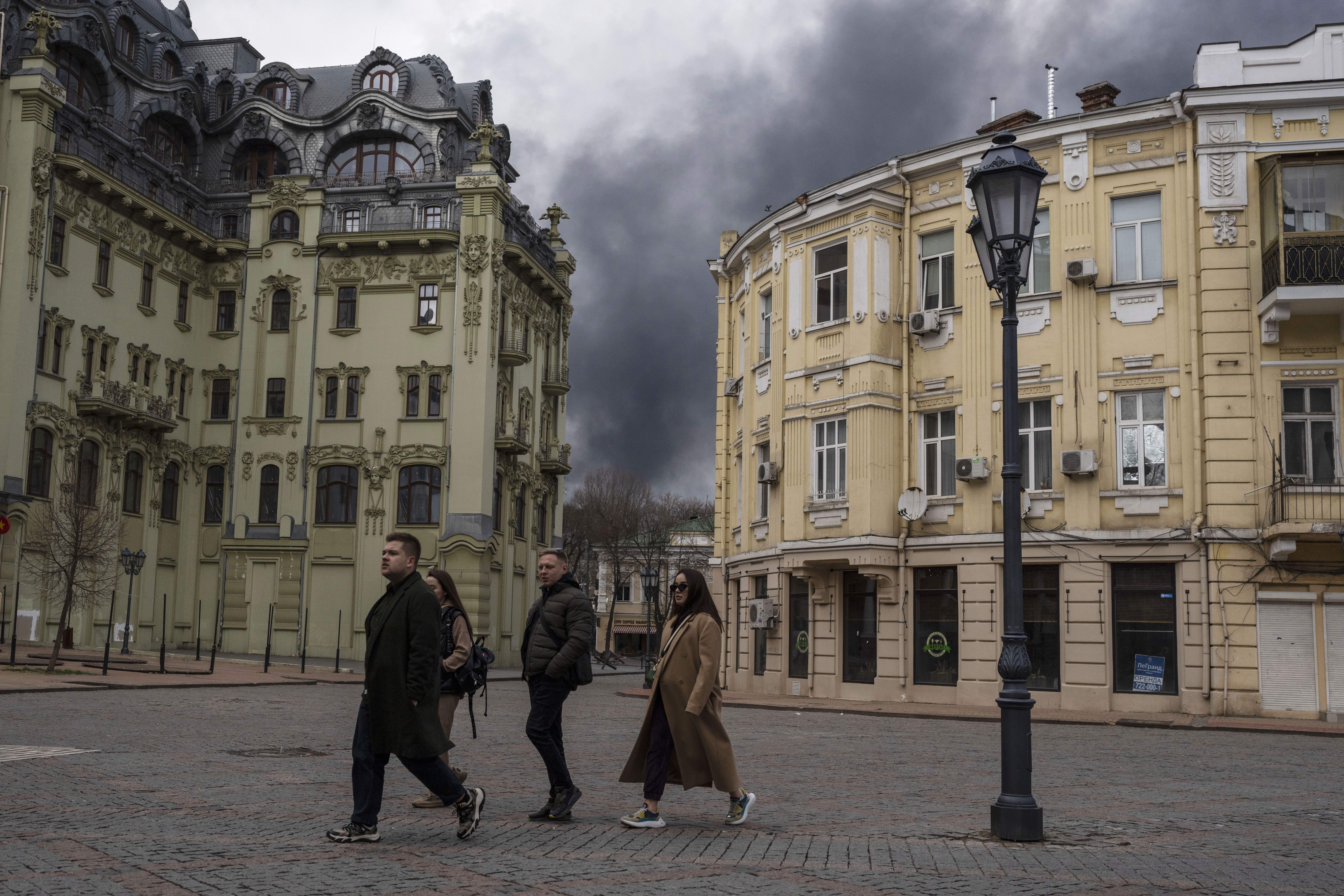 People walk in the street as smoke rises.