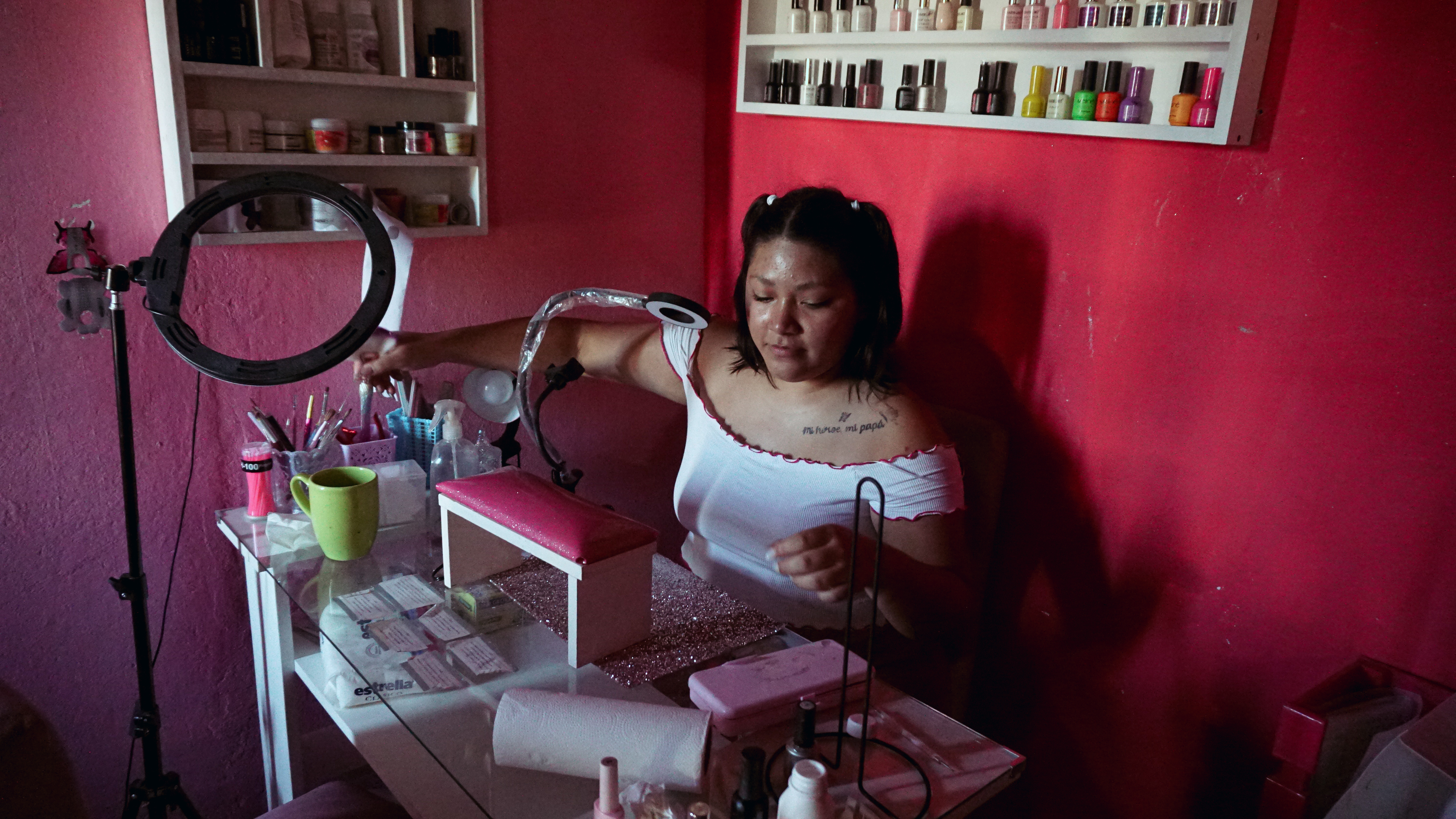 A photo of a woman sitting behind a table with manicure accessories and tools.