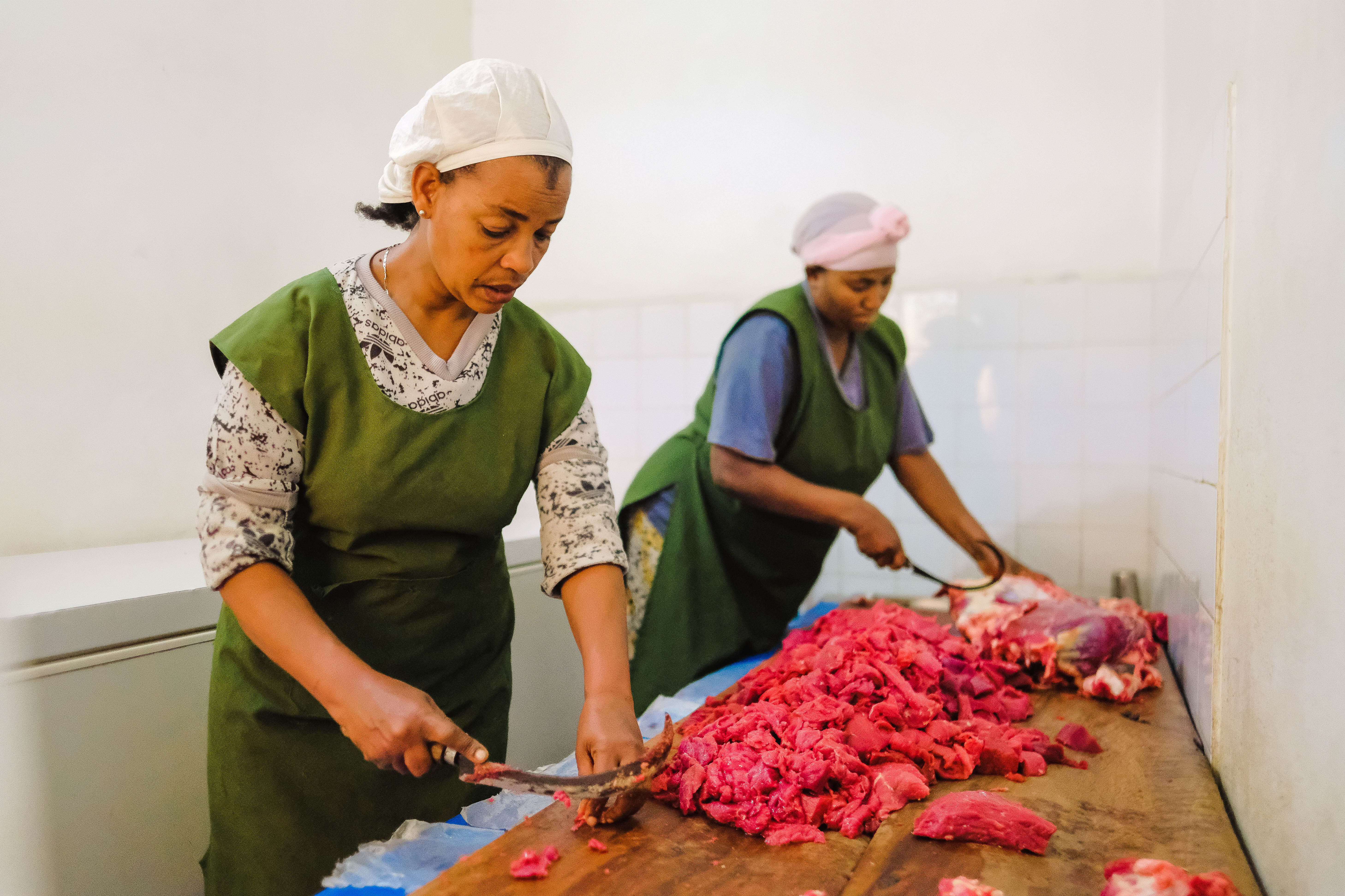 Two cooks use special lekema knives to clean the meat