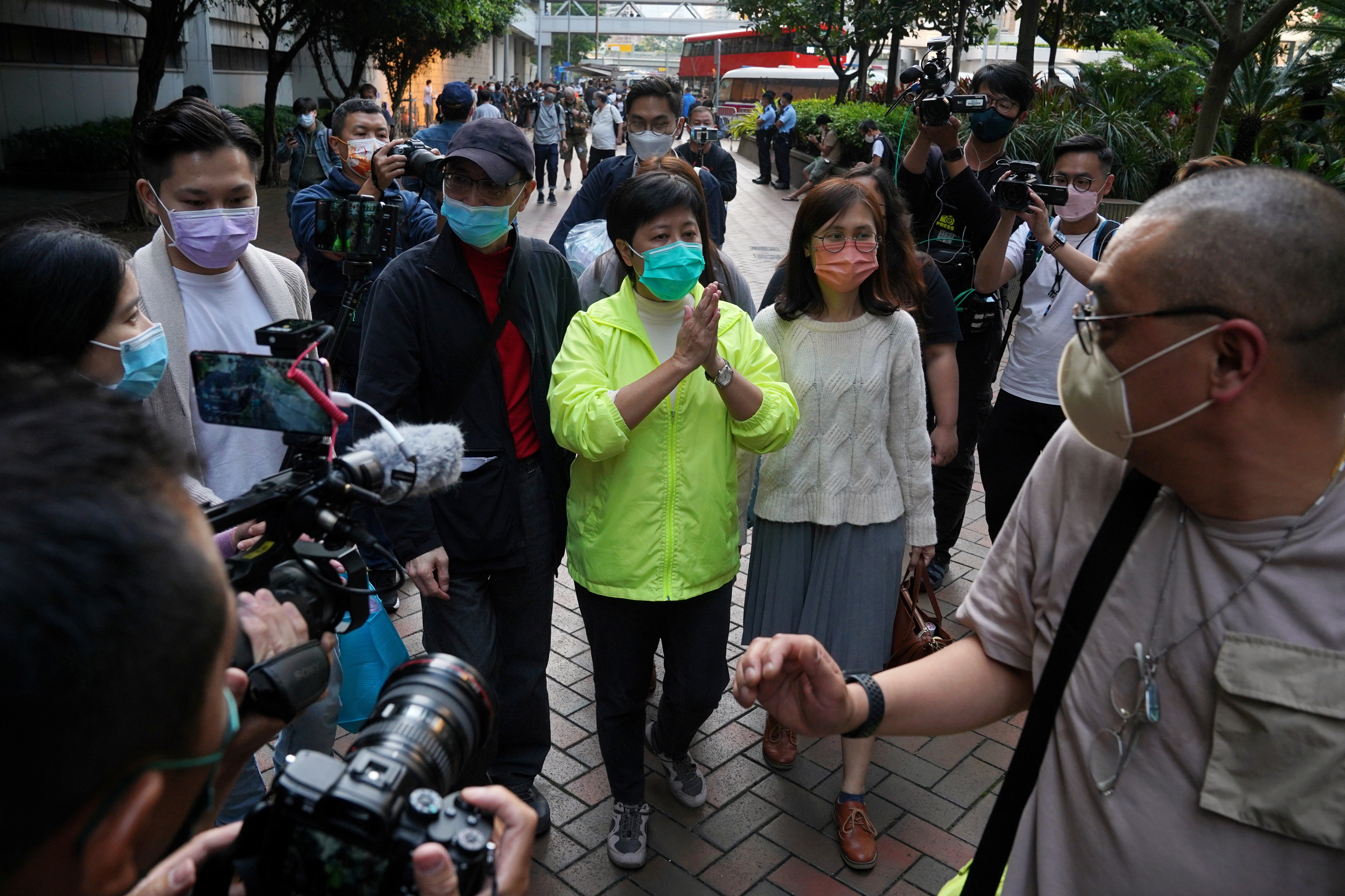 Former lawmaker Helena Wong Pik-wan appears outside court after a prosecution appeal against her being given bail was rejected. She's wearing a lime green t-shirt and has her hands clasped together in thanks. She is accompanied by another woman. Media are around her.