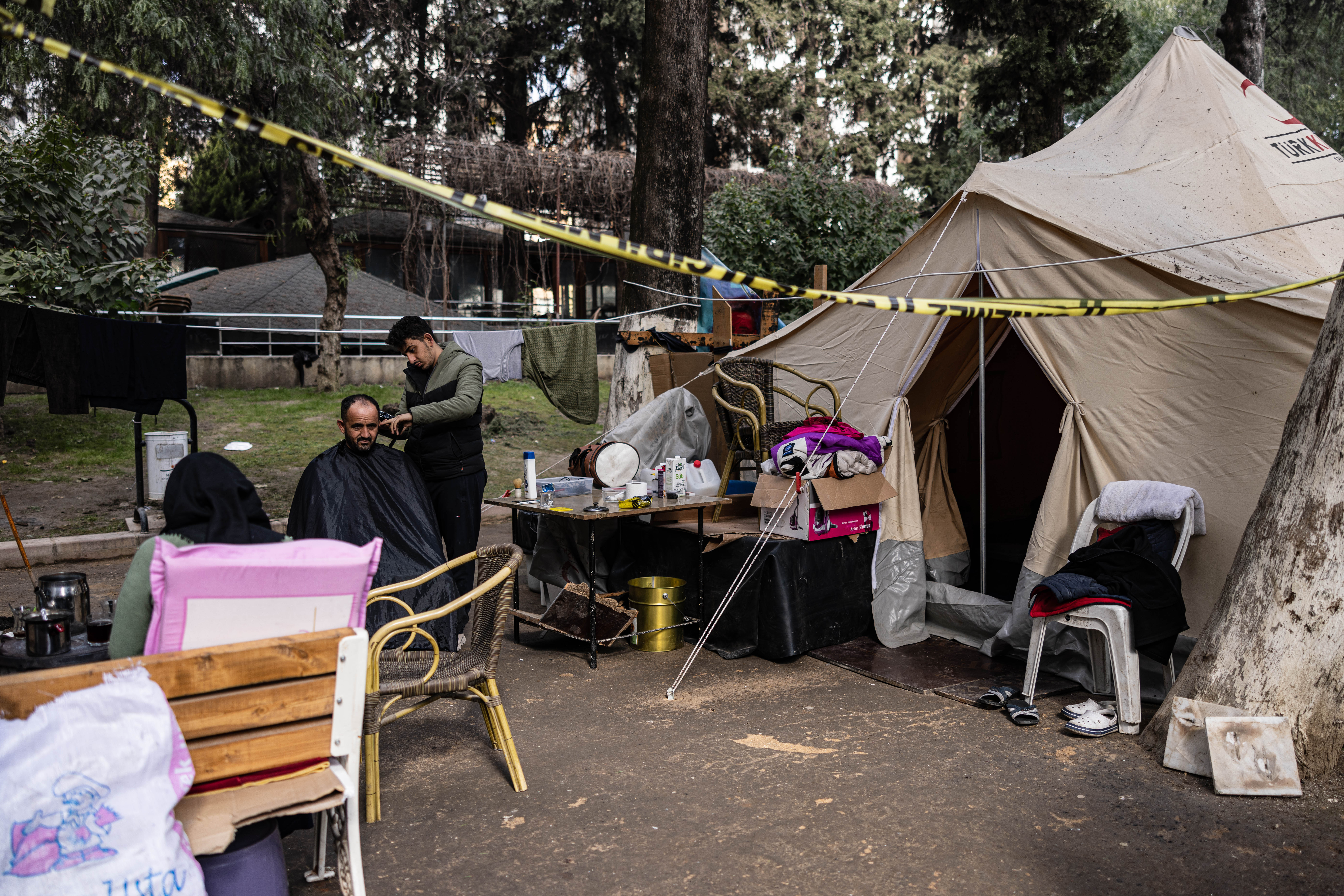 Eighteen-year-old Syrian Mohammed al-Hamo (R) cuts the hair of his father Khaled (L) in front of their tent at a makeshift camp in the city of Antakya on February 19, 2023. - A 7.8-magnitude earthquake hit near Gaziantep, Turkey, in the early hours of February 6, followed by another 7.5-magnitude tremor just after midday. The quakes caused widespread destruction in southern Turkey and northern Syria and has killed more than 44,000 people. (Photo by Sameer Al-DOUMY / AFP)