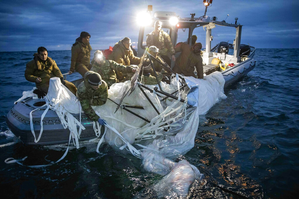Several US navy personnel in army gear on a boat pull in the white material of the large balloon.