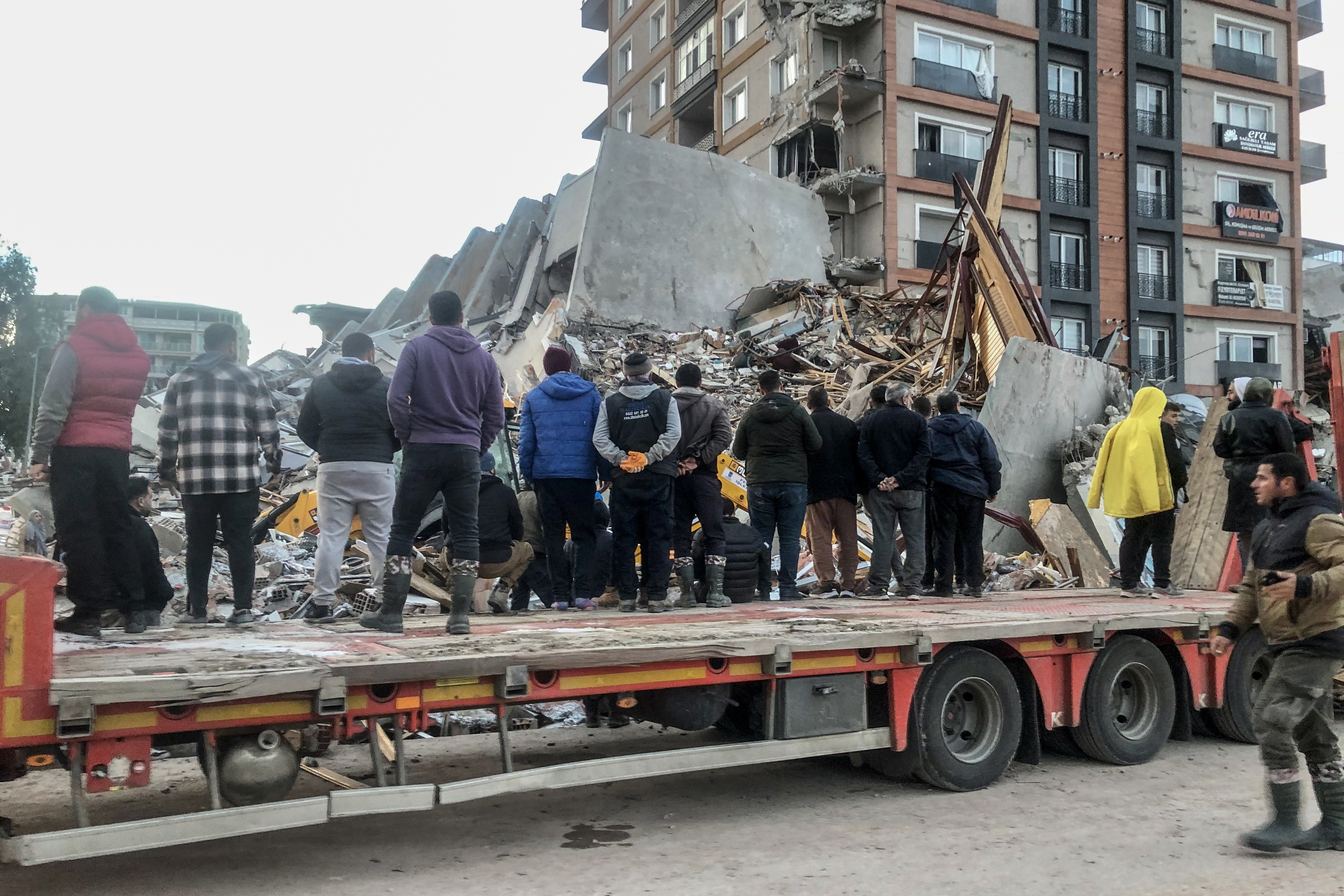 people stand in front of rubble in antakya