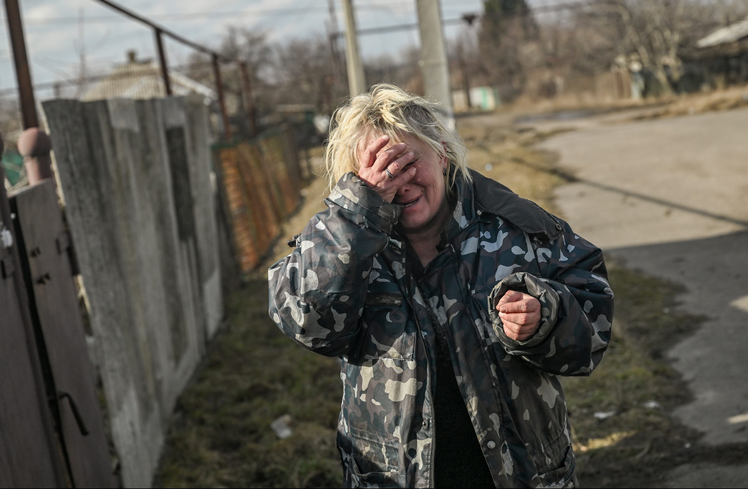 A woman reacts to the sound of shelling as she stands outside her house in the village of Chasiv Yar