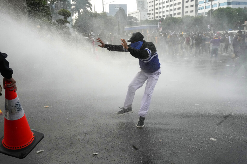A student reacts as police use a water cannon to disperse protesters during a rally outside the parliament in Jakarta, Indonesia, Monday, April 11, 2022. Thousands of students marched in cities around Indonesia on Monday to protest against rumors that the government is considering postponing the 2024 presidential election to allow President Joko Widodo to remain in office beyond the two-term legal limit, calling it a threat to the country's democracy. (AP Photo/Tatan Syuflana)