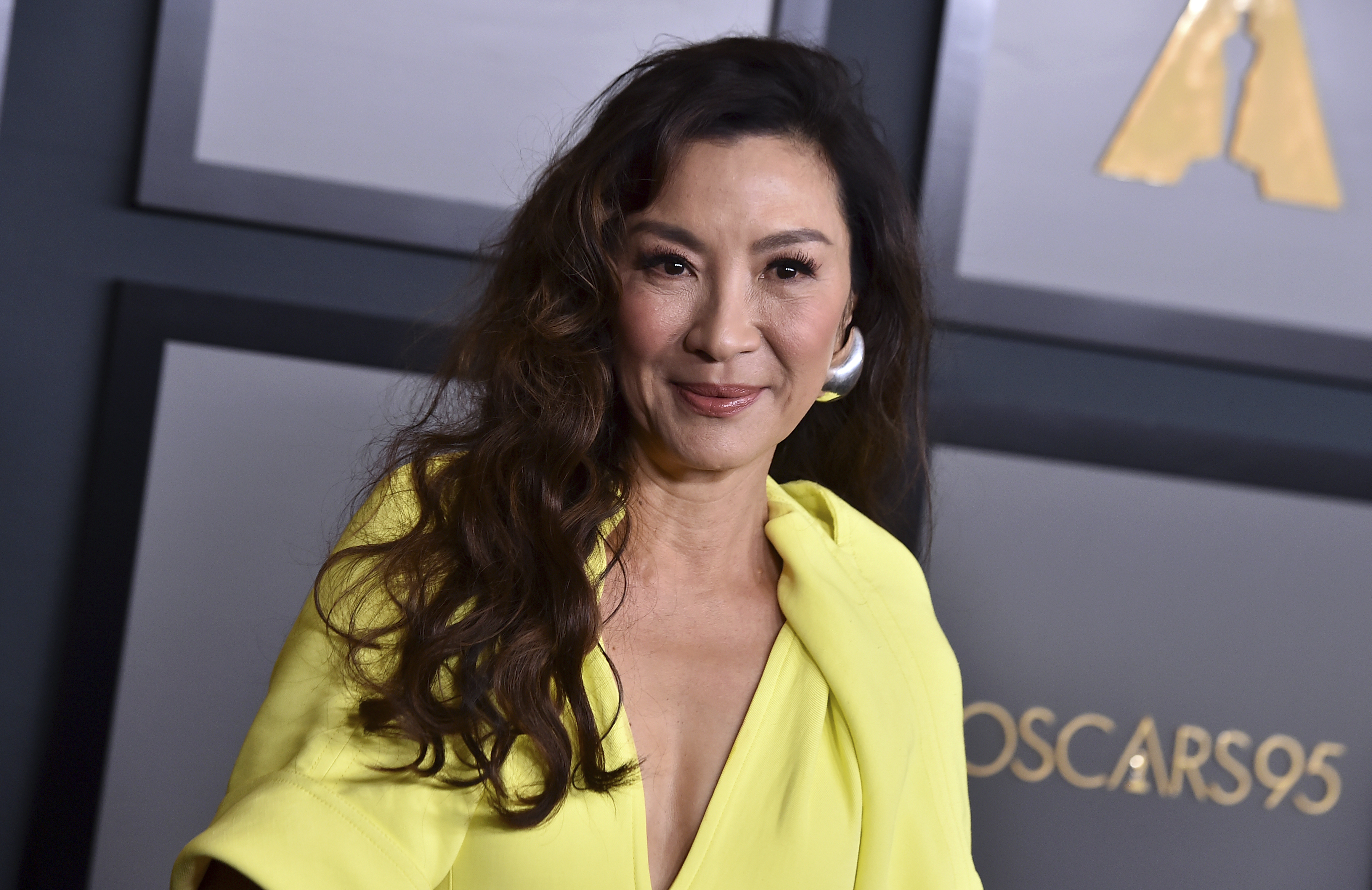 Michelle Yeoh pictured at an Oscar's event. She's wearing a yellow evening gown and smiling.