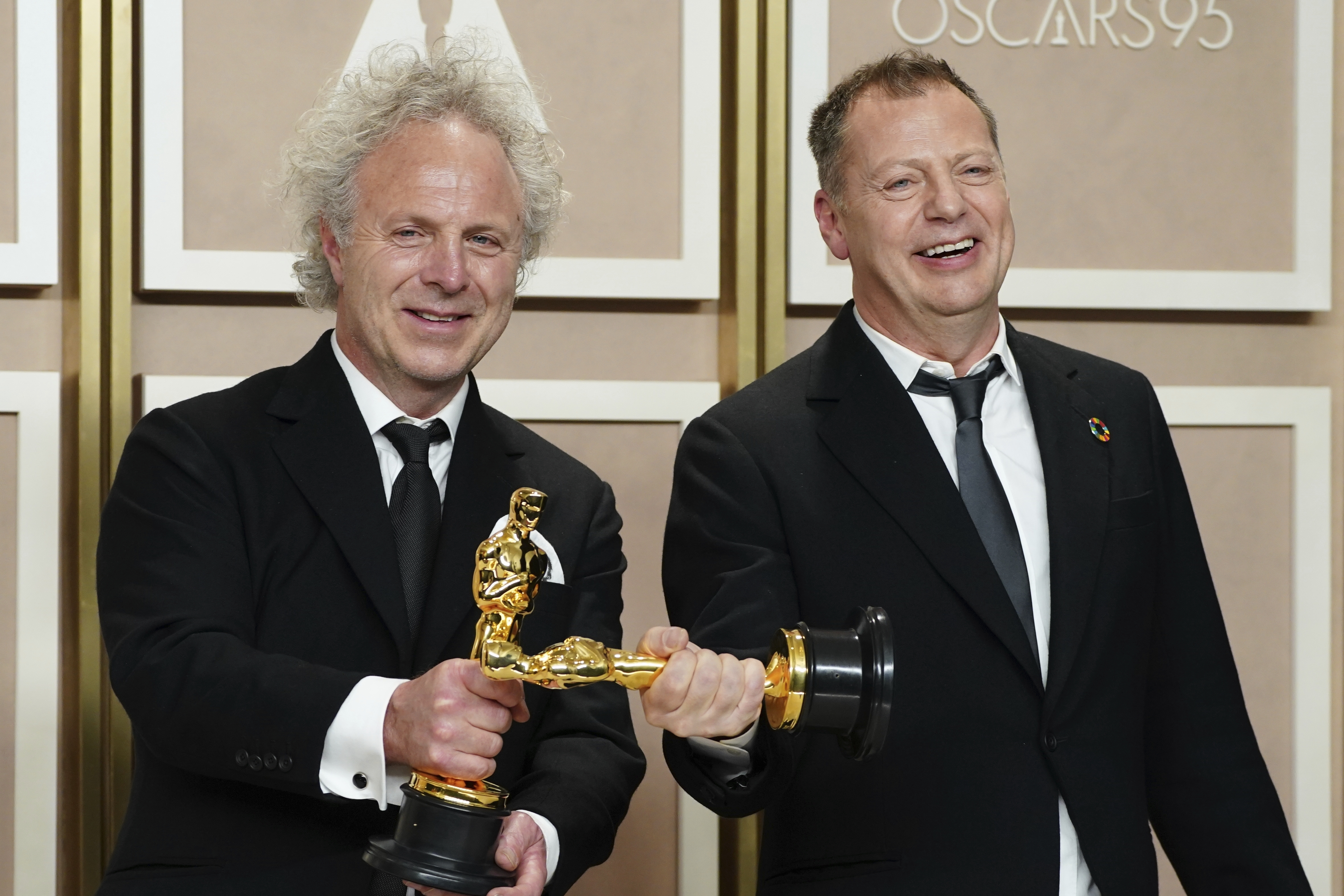 Two men hold their Oscars perpendicular to one another