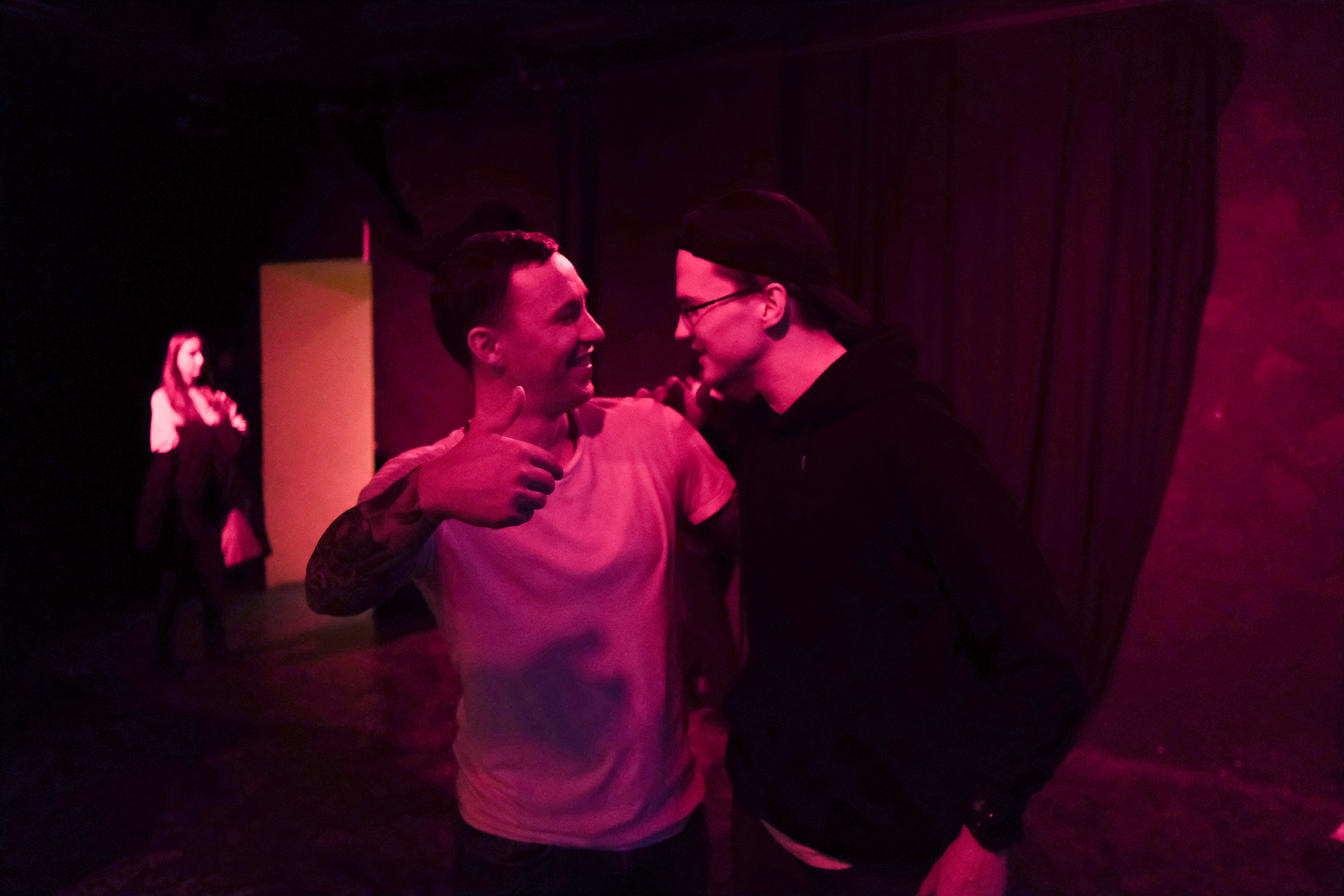 A photo of two people standing next to each other with someone in a door behind them.