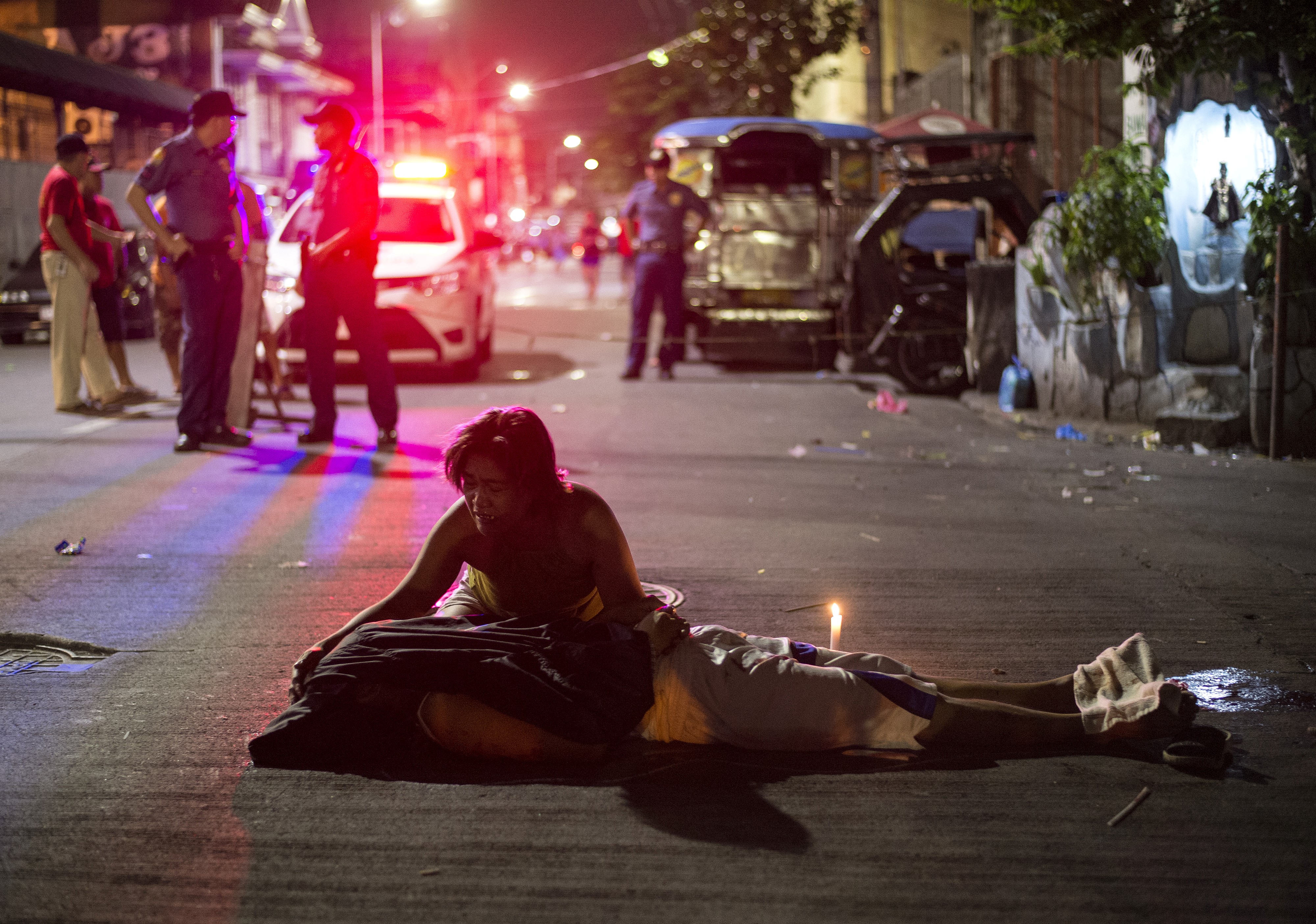 Nanette Castillo grieves over the body of her son. She is kneeling beside him in the street, There are red and blue lights behind and a crowd of people. Her son's face is covered.