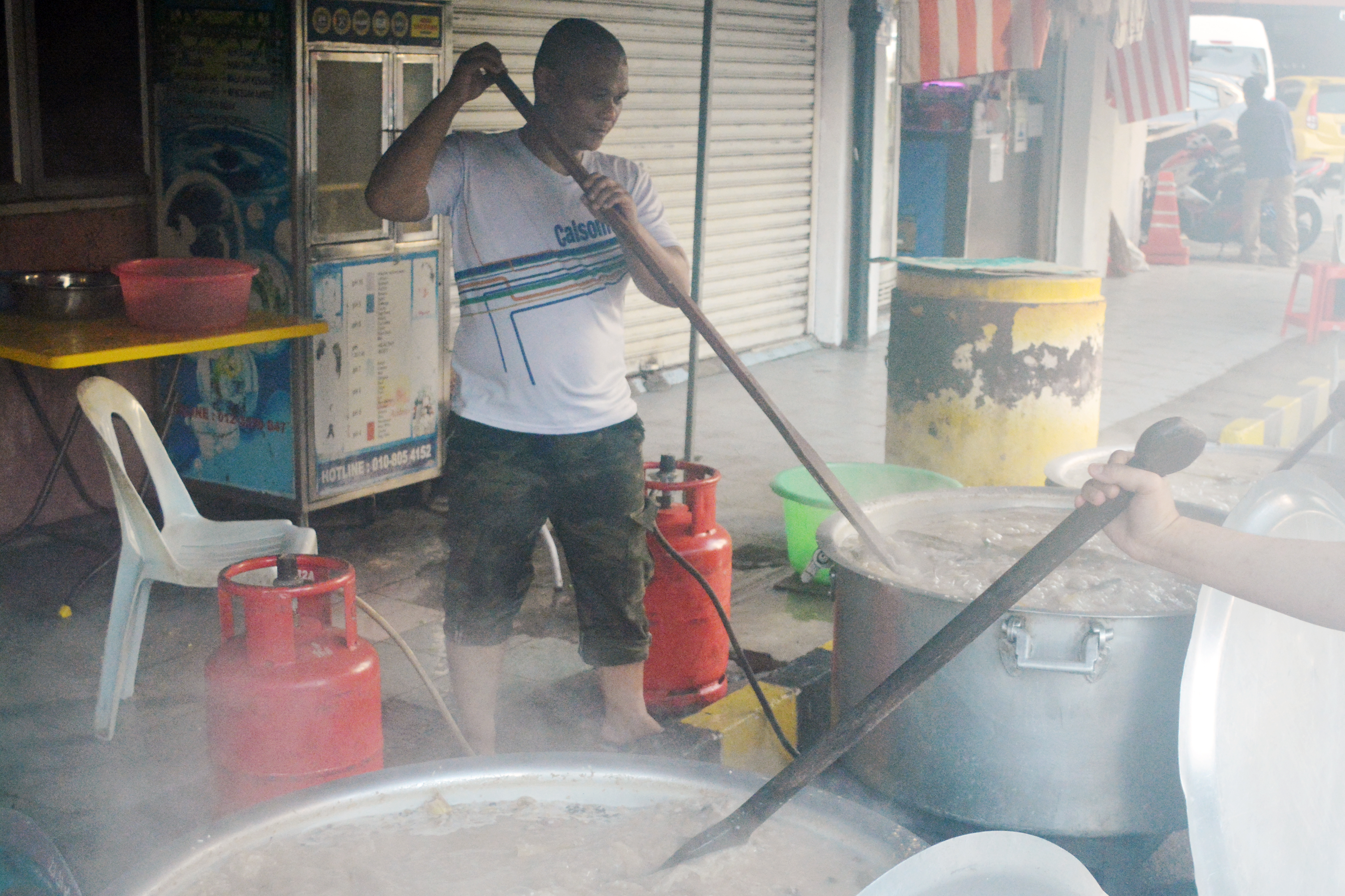 Saiful Azrul (L), and his brothers cook three pots of Bubur Lambuk (Malaysian Porridge)—one for charity, and two for selling.