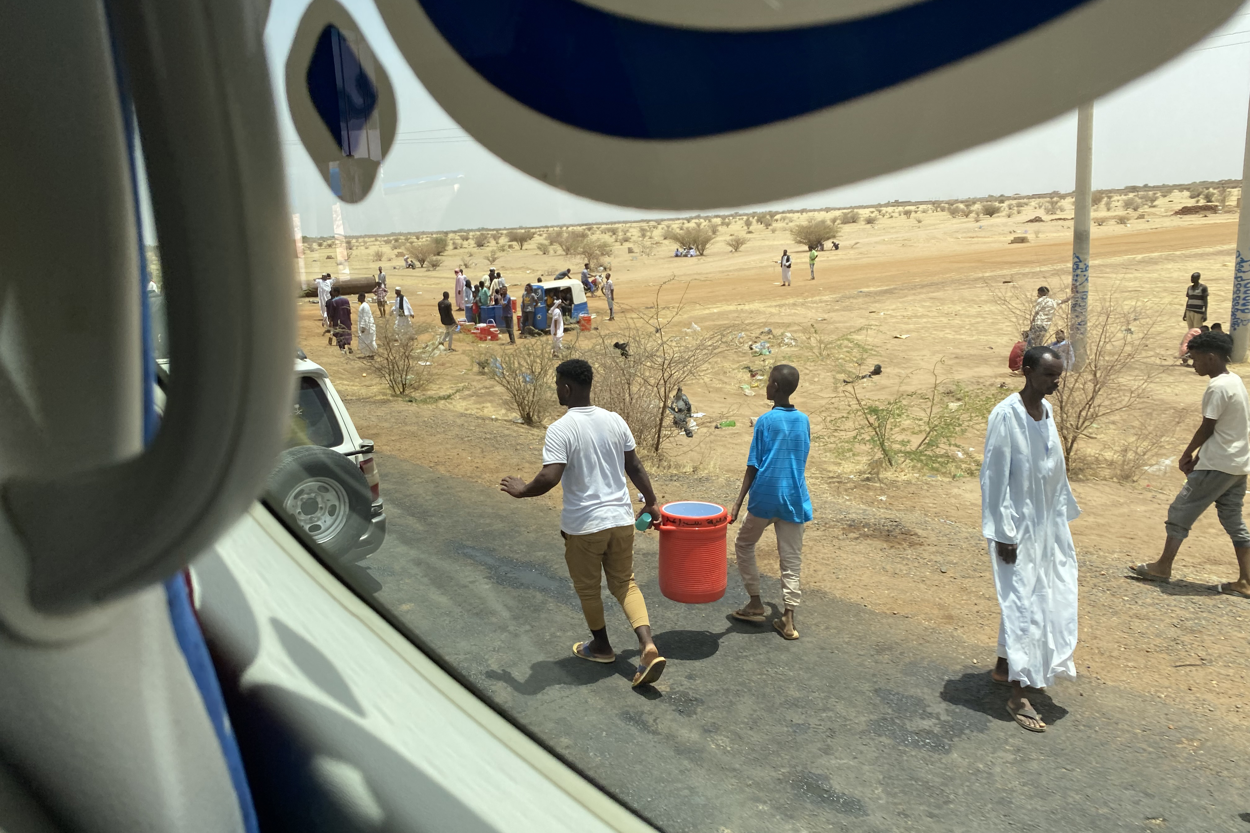 People with big coolers of karkade and water run alongside the buses