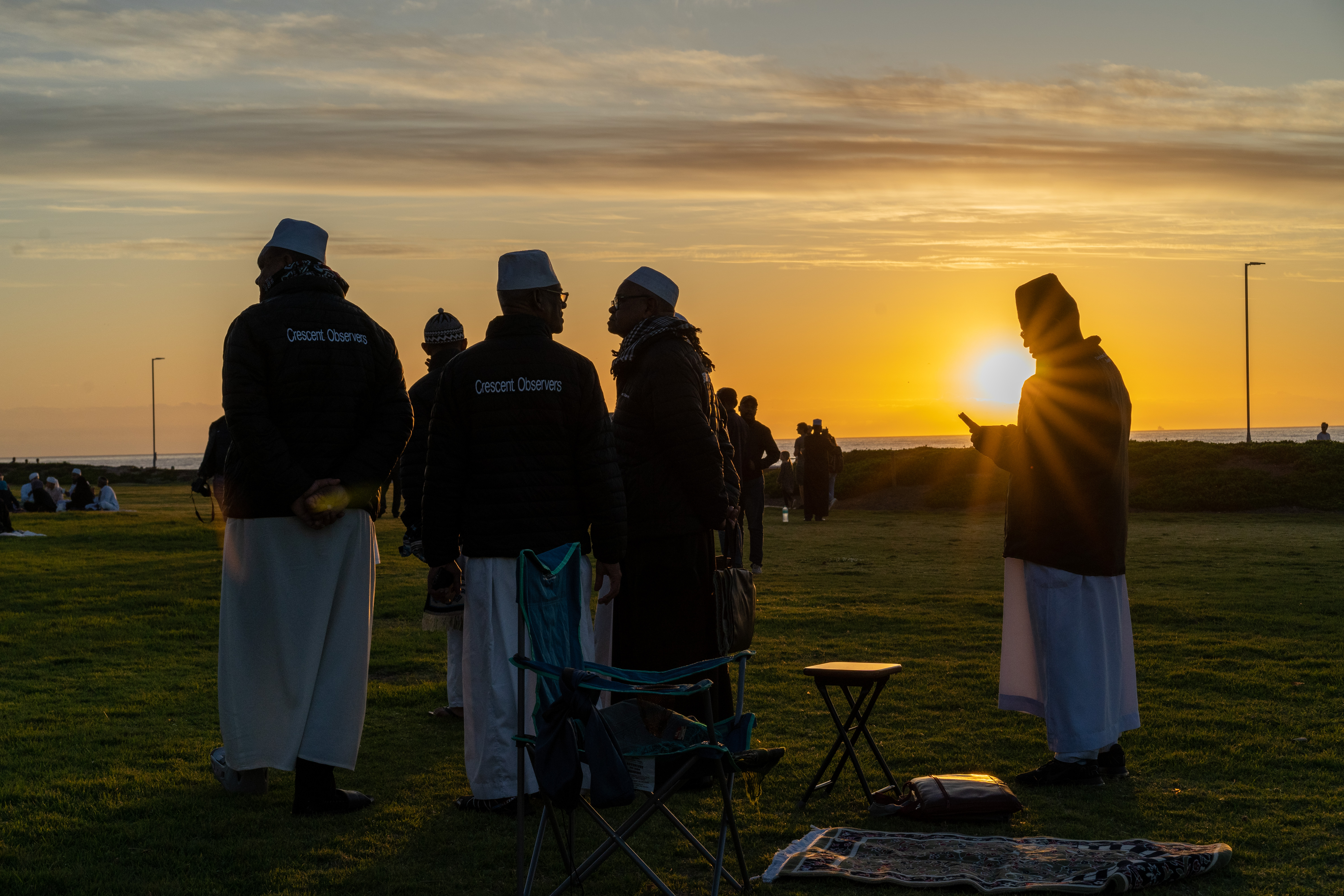 A photo of a group of people standing in a grassy area during a sunset.