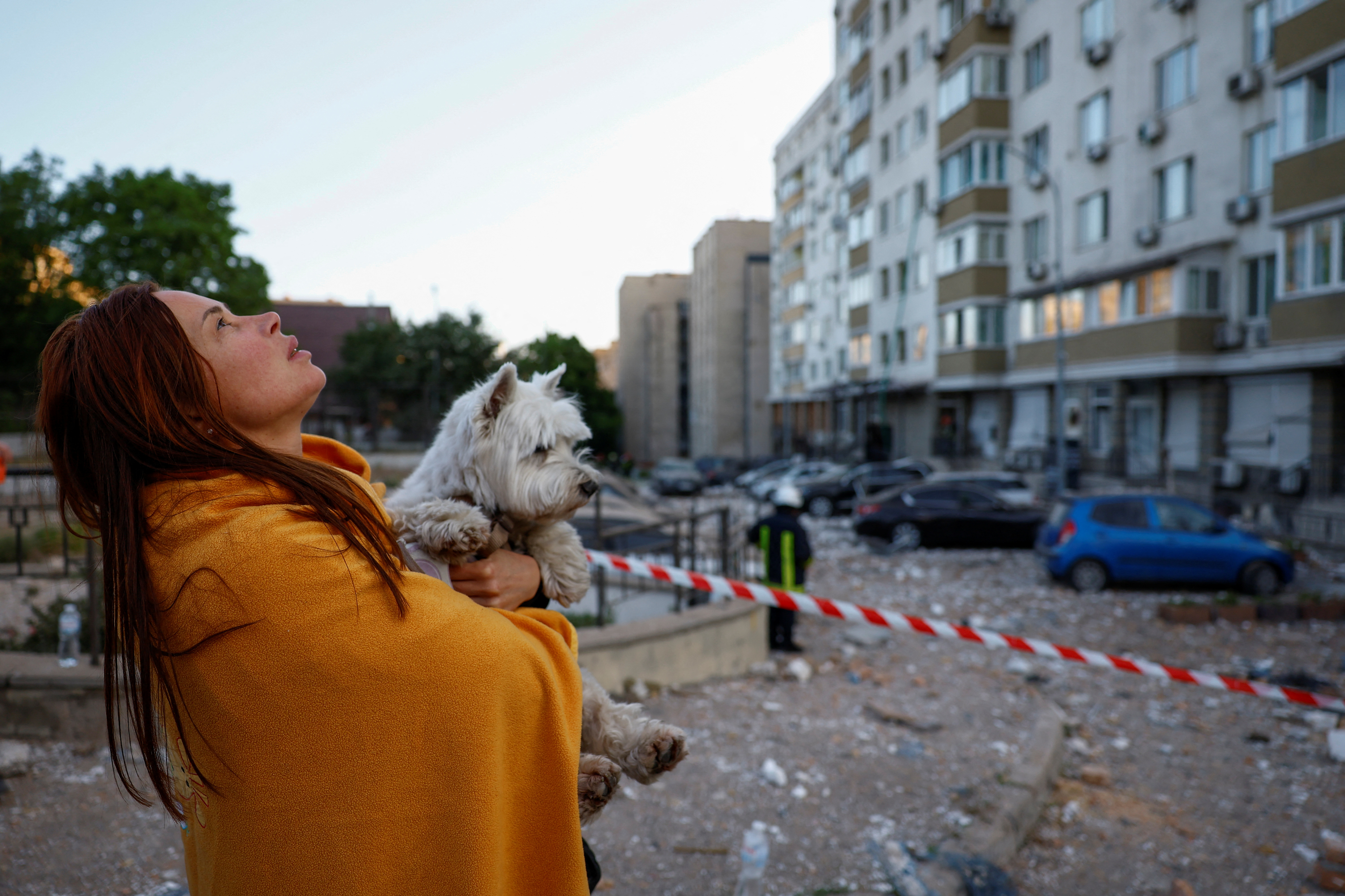 A woman with a dog looks at her apartment building heavily damaged during a massive Russian drone strike