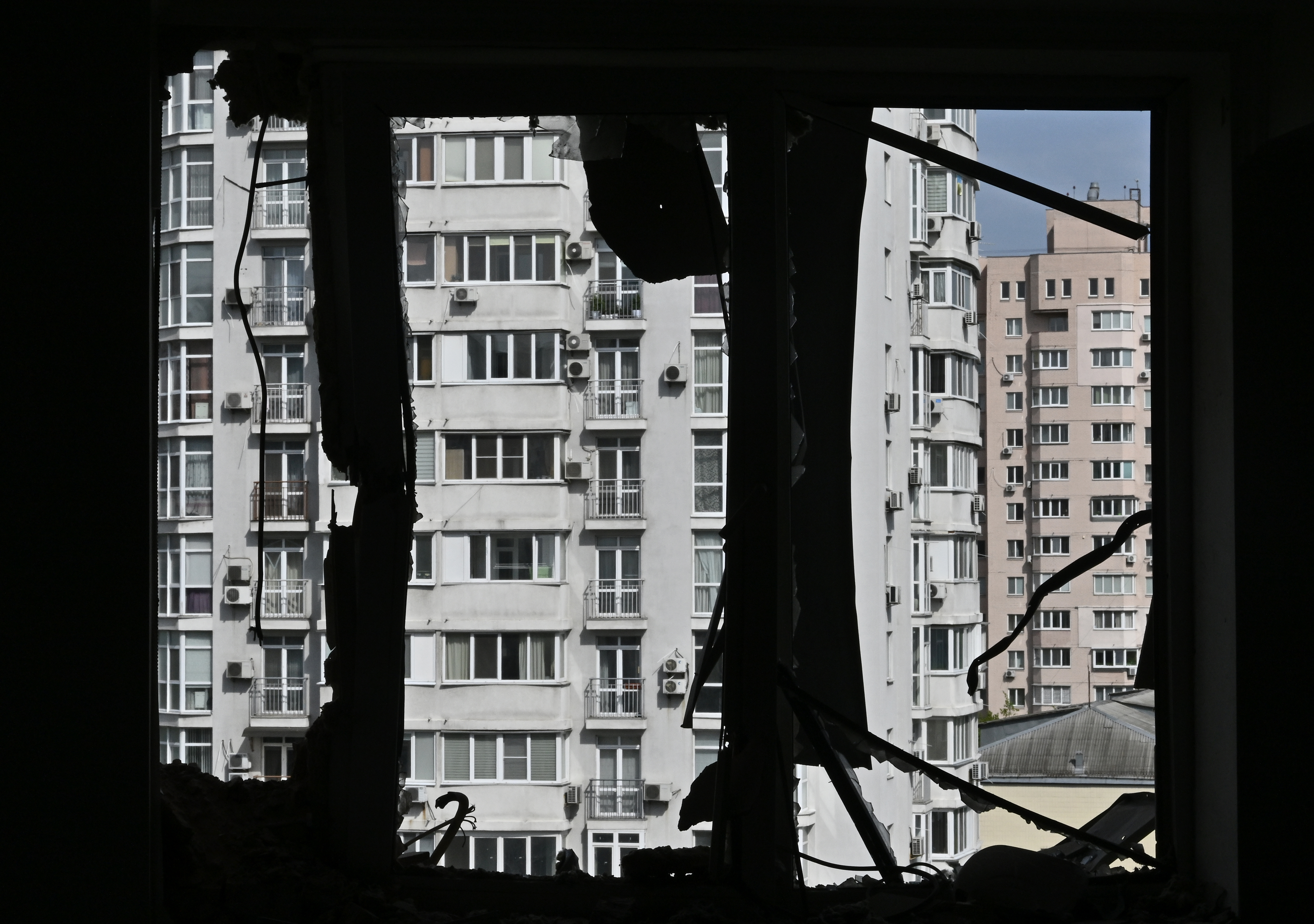 The view from the window of a heavily damaged flat in Kyiv. The window is silhouetted. There are other buildings behind.