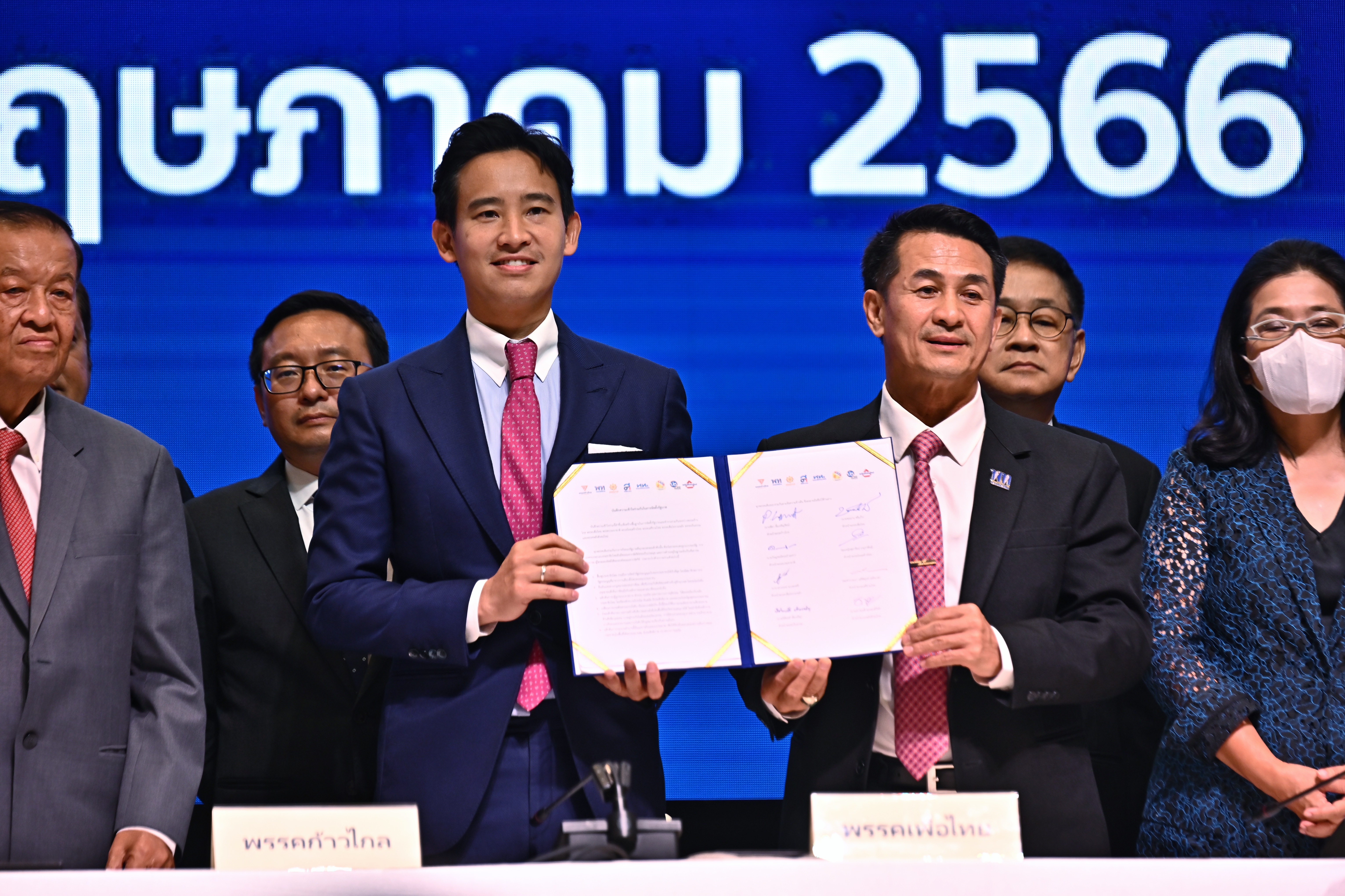 Move Forward Party leader Pita Limjaroenrat and Pheu Thai Party leader Cholanan Srikaew hold a memorandum of understanding signed by eight Thai political parties in agreement to form a new government. They are both dressed in suits and smiling.