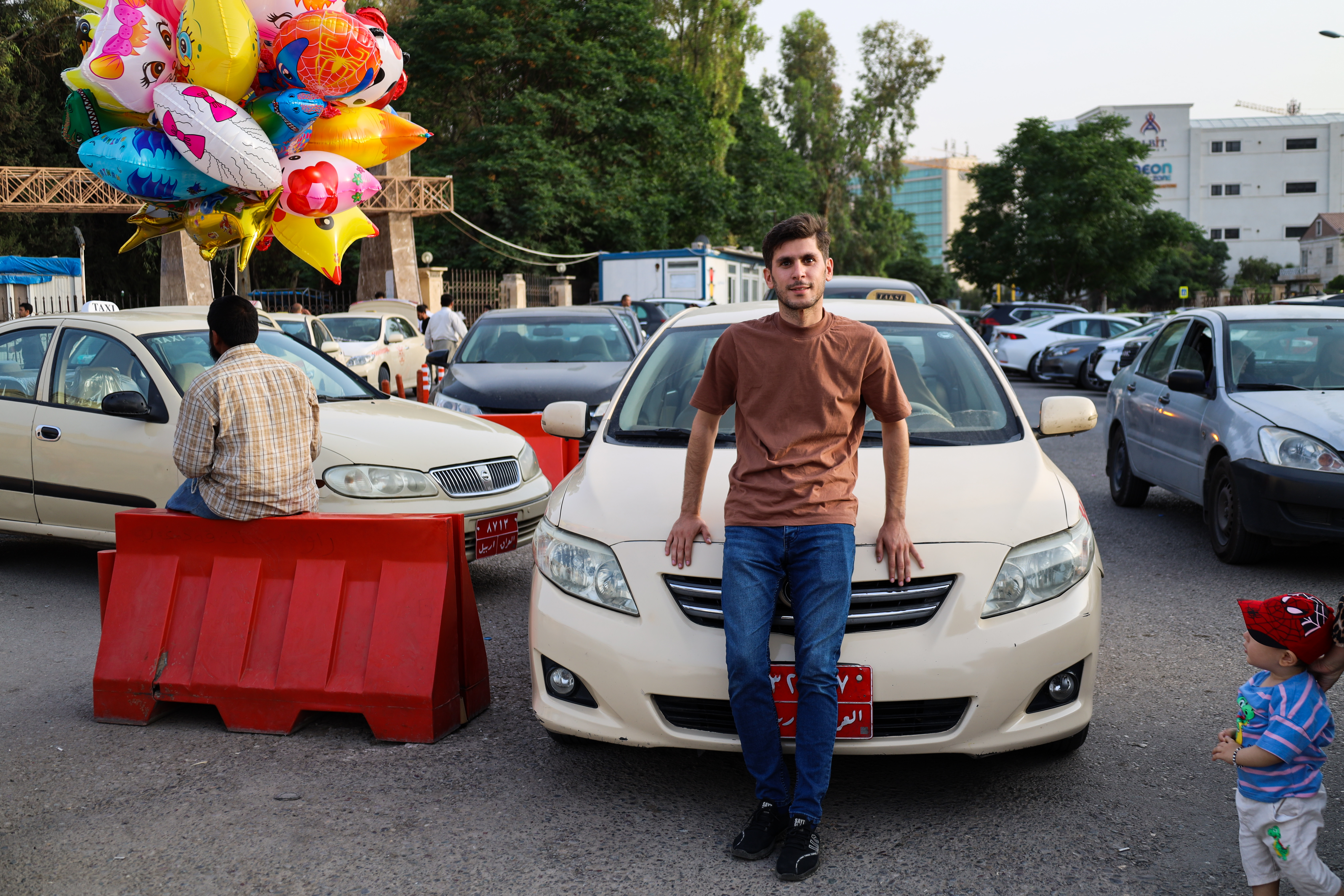 A photo of Mumen standing in front of his taxi by the entrance to Sami Abdulrahman Park.