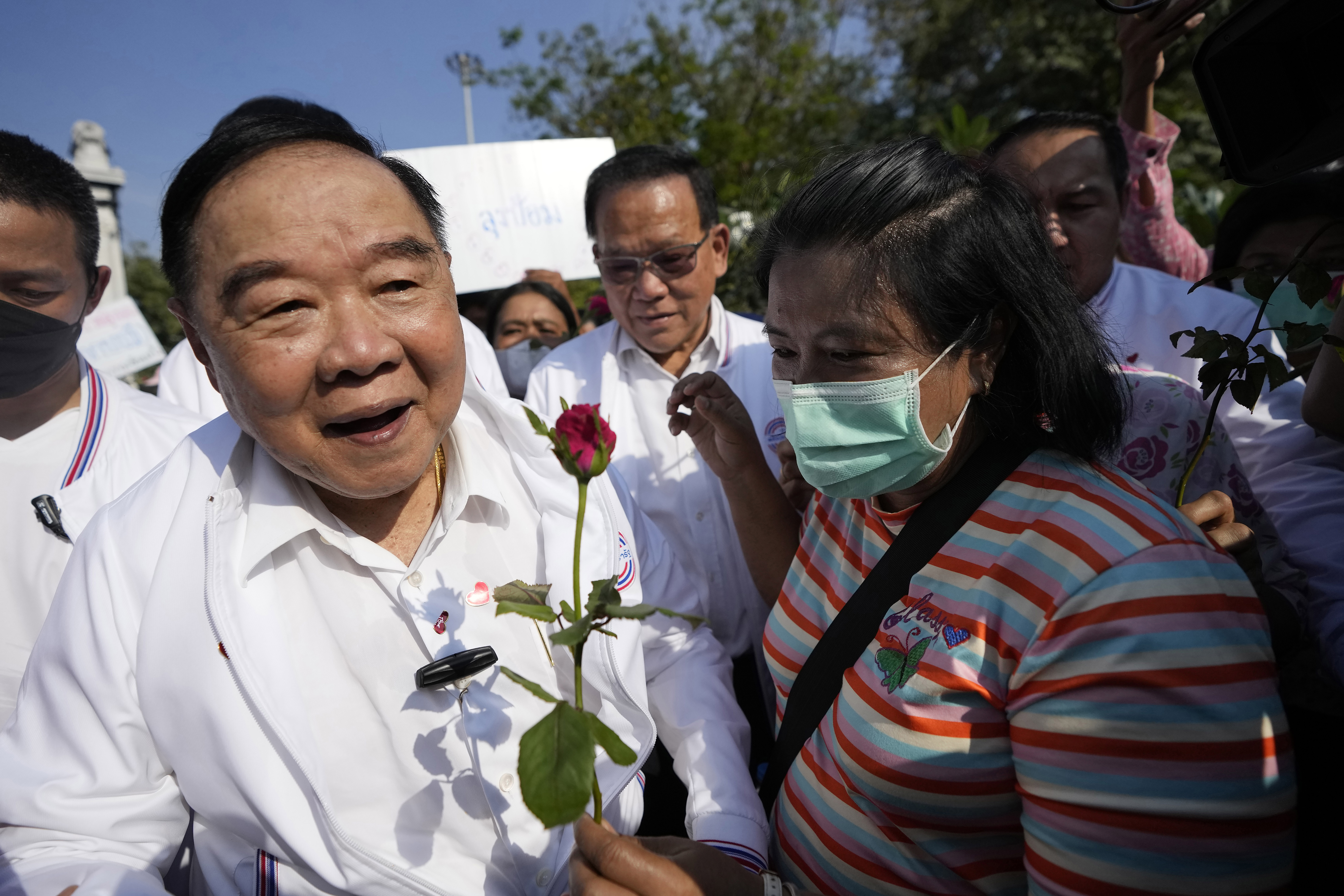 Prawit Wongsuwan greeting supporters. He's wearing a white shirt and looks happy. He's being given a red rose 