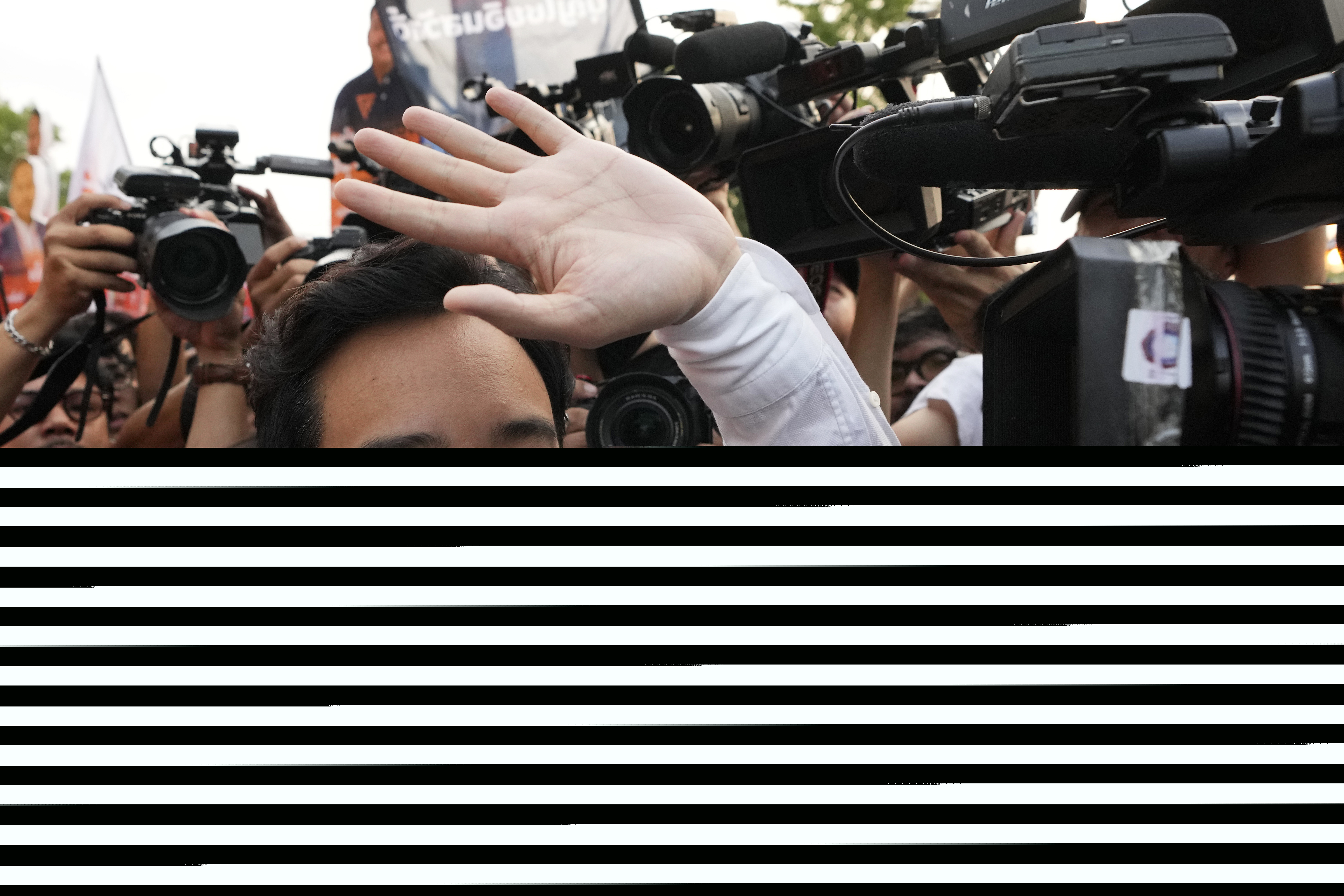 Pita Limjaroenrat waves to supporters. He is smiling and wearing a white shirt.