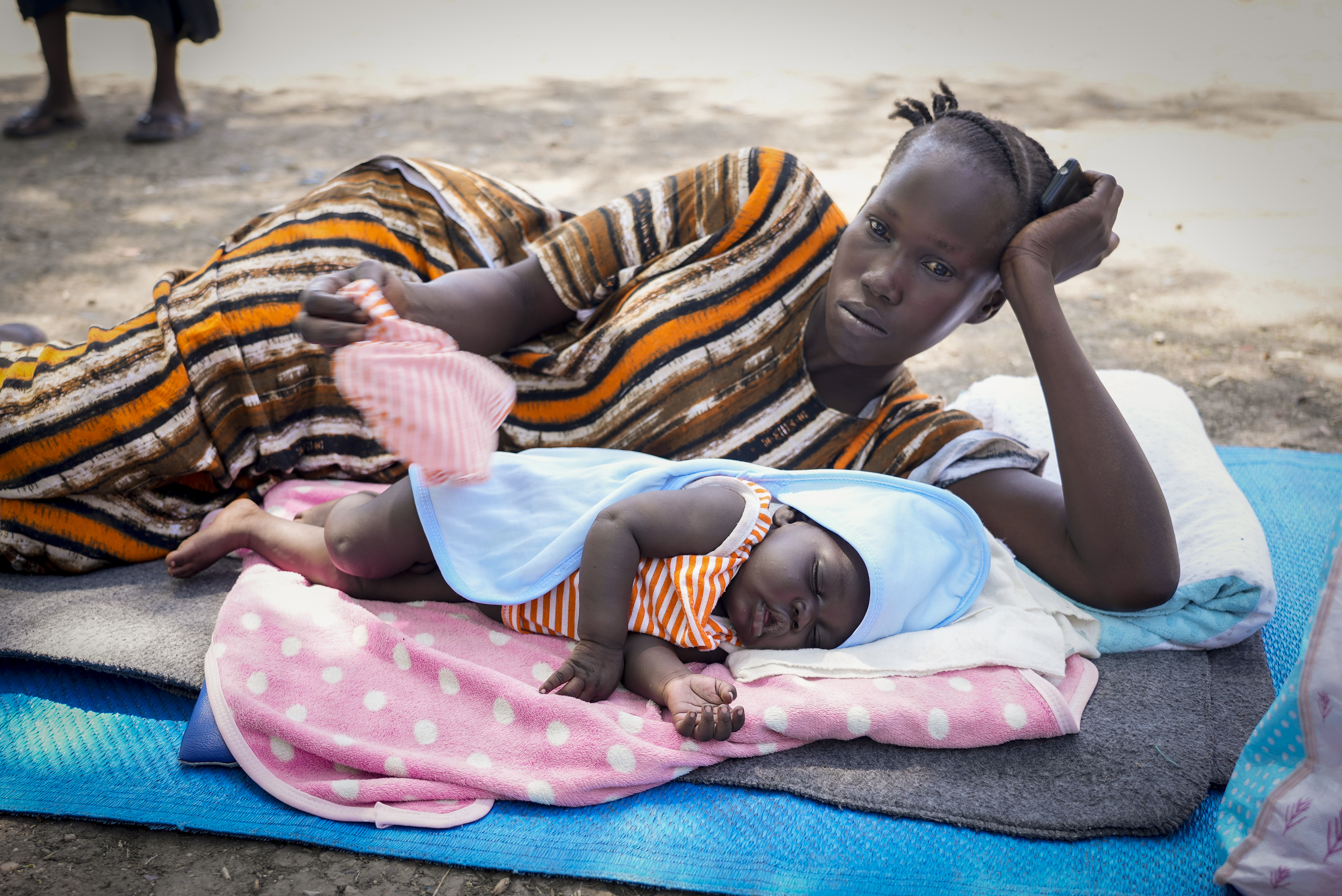 A South-Sudanese woman who fled fighting in Sudan lies on the ground with her child under a tree after returning to Malakal town, which is hosting thousands who returned, in Upper Nile state, South Sudan