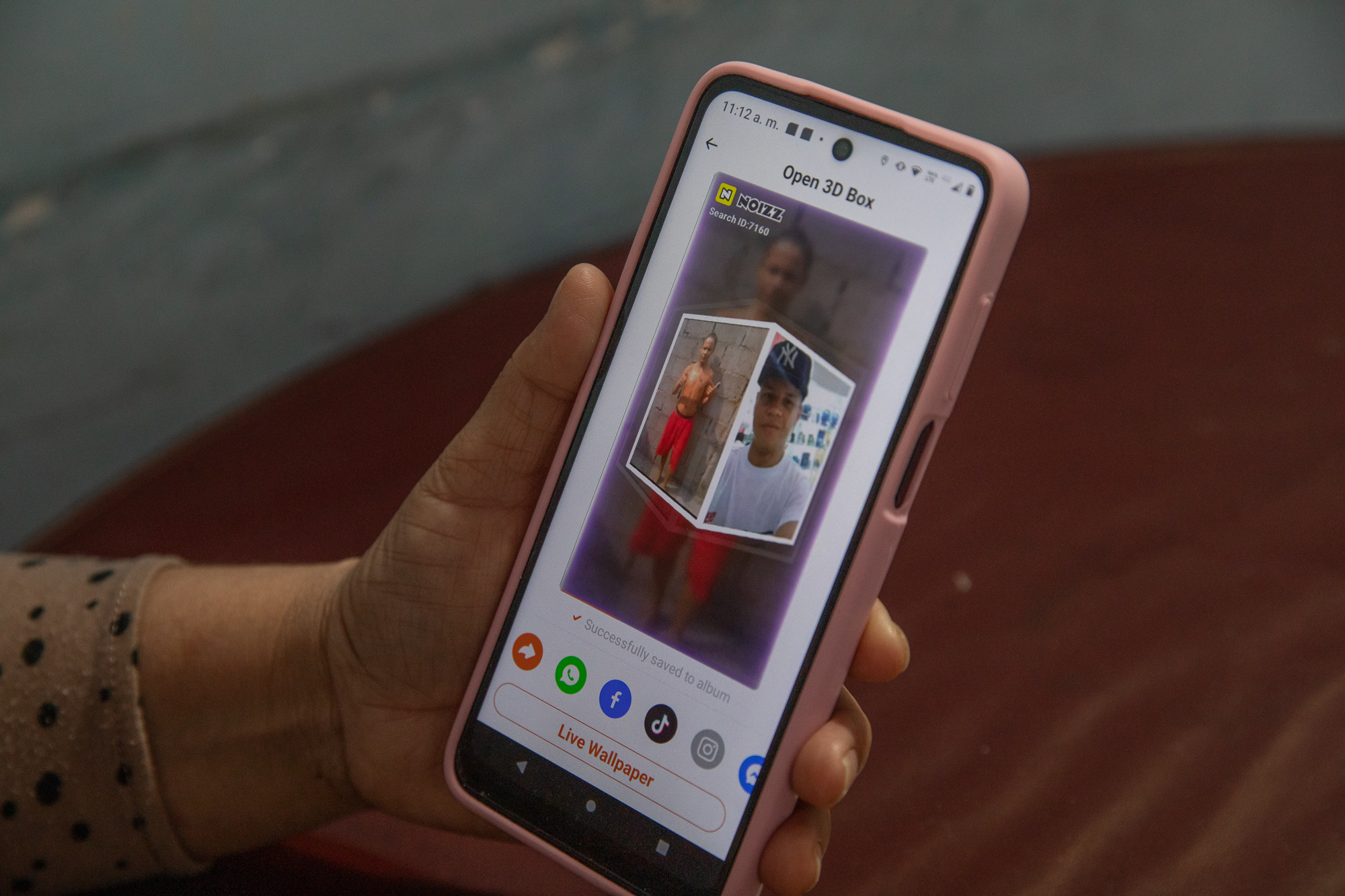 A hand holds a telephone screen, featuring the face of a young man.