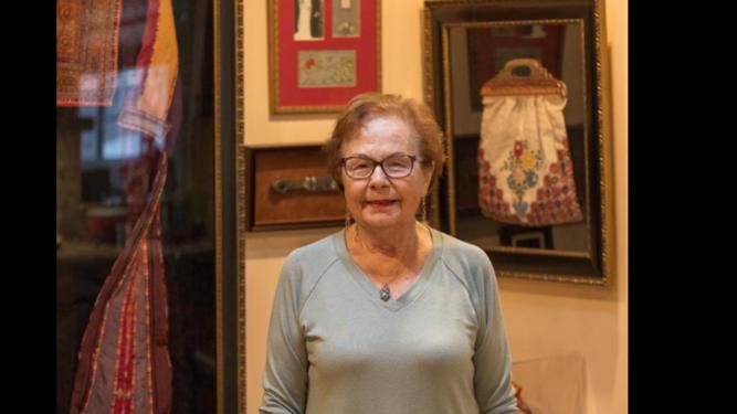 Leila Giries stands in front of framed items such as the bag her mother used when fleeing during the Nakba