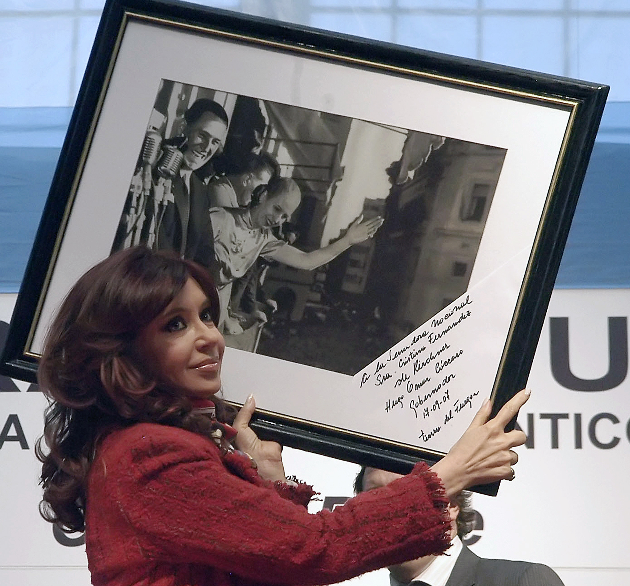 A woman in a red suit hoists a large framed photograph up on one shoulder