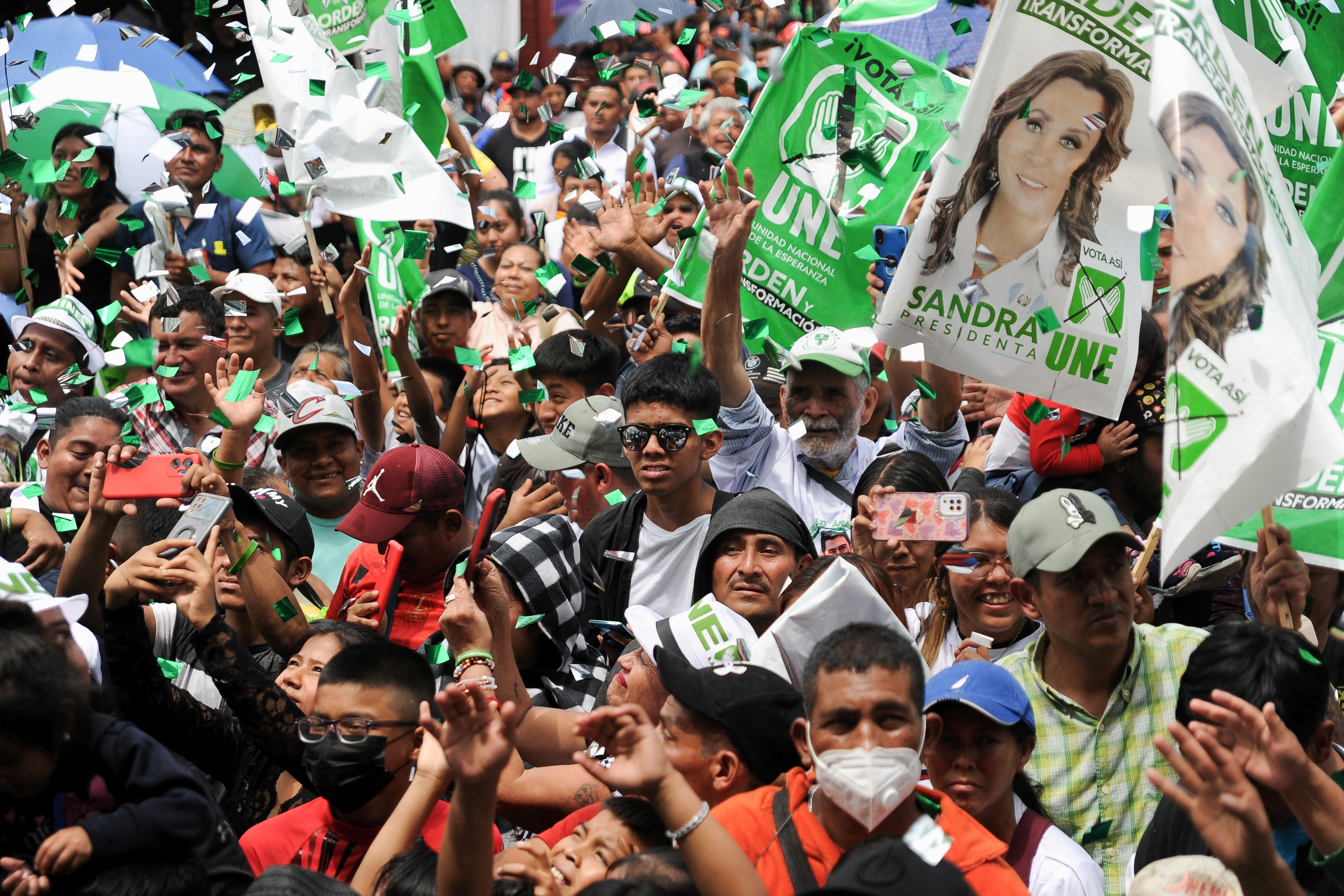 Confetti falls as a packed crowd raises their arms and carries banners featuring Sandra Torres's picture, as well as party slogans.