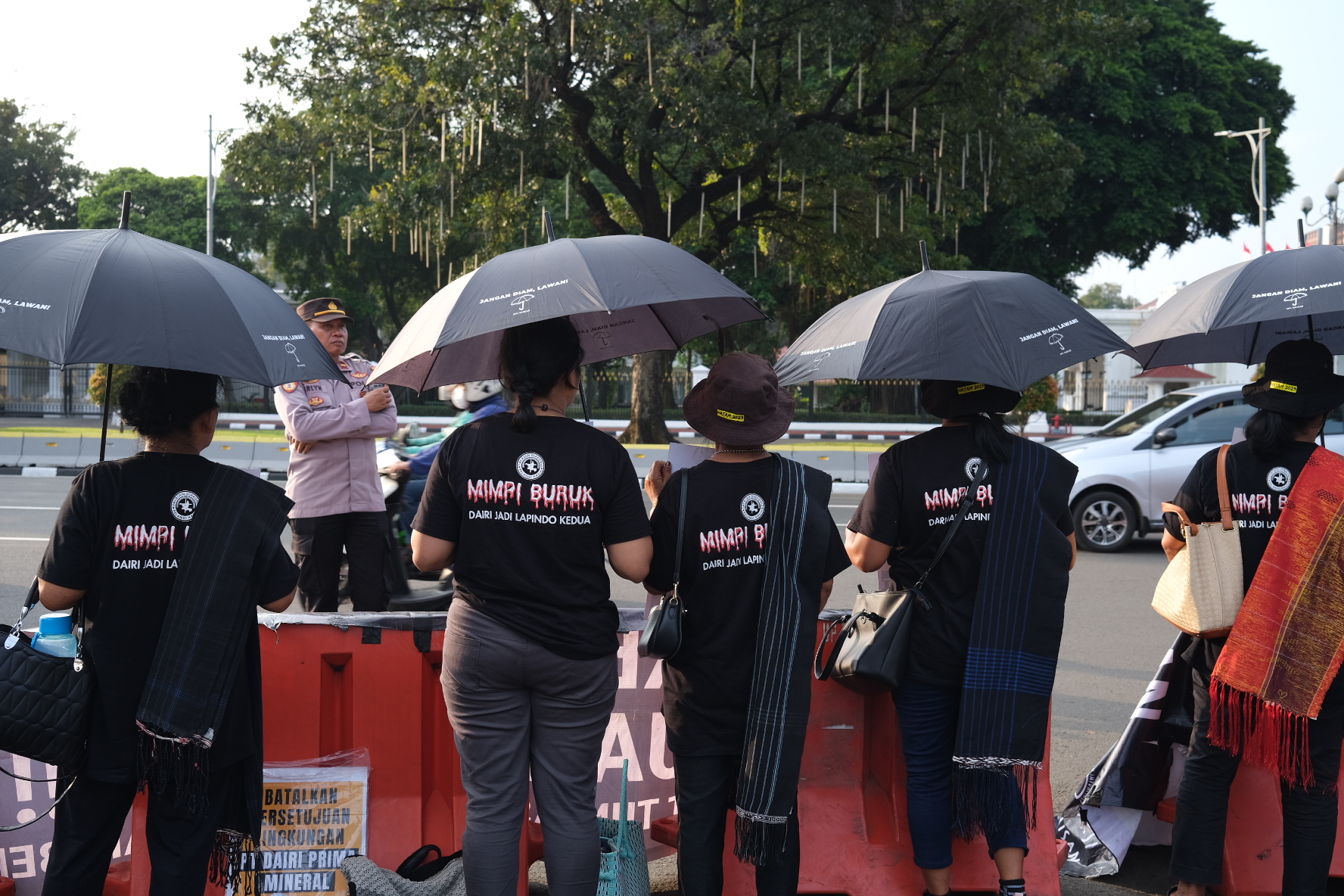 Demonstrators standing beneath black umbrellas. They are on the road opposite the presidential palace in Jakarta. They are wearing T-shirts reading 'dark dreams' on the back