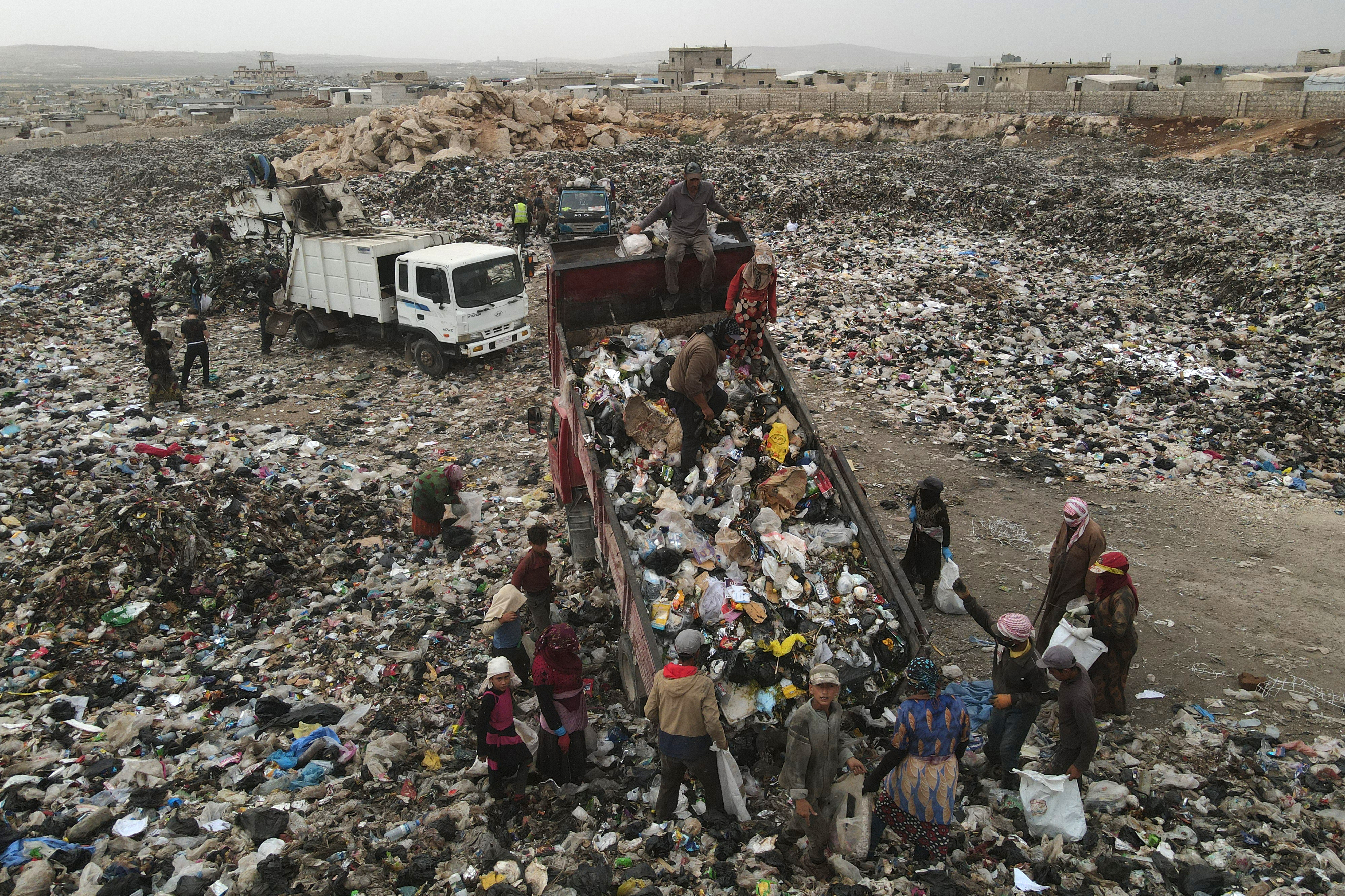 In this picture taken on June 3, 2023, people surround rubbish trucks as they unload at a dump site, to collect plastic items to sell for recycling, near the village of Hazreh in Syria's northwestern Idlib province.