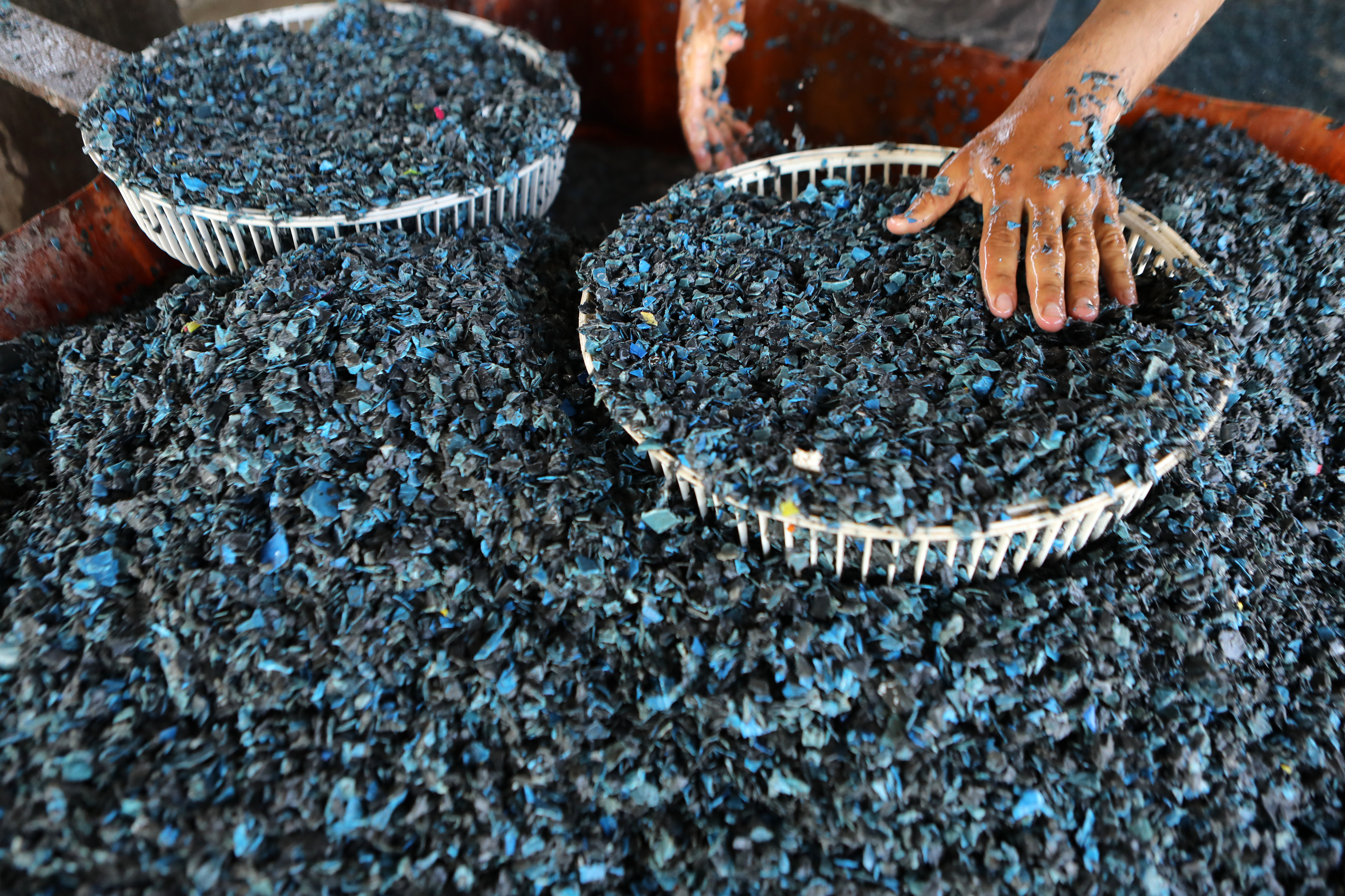 a worker washes plastic gathered from dump sites after being crushed into small pieces