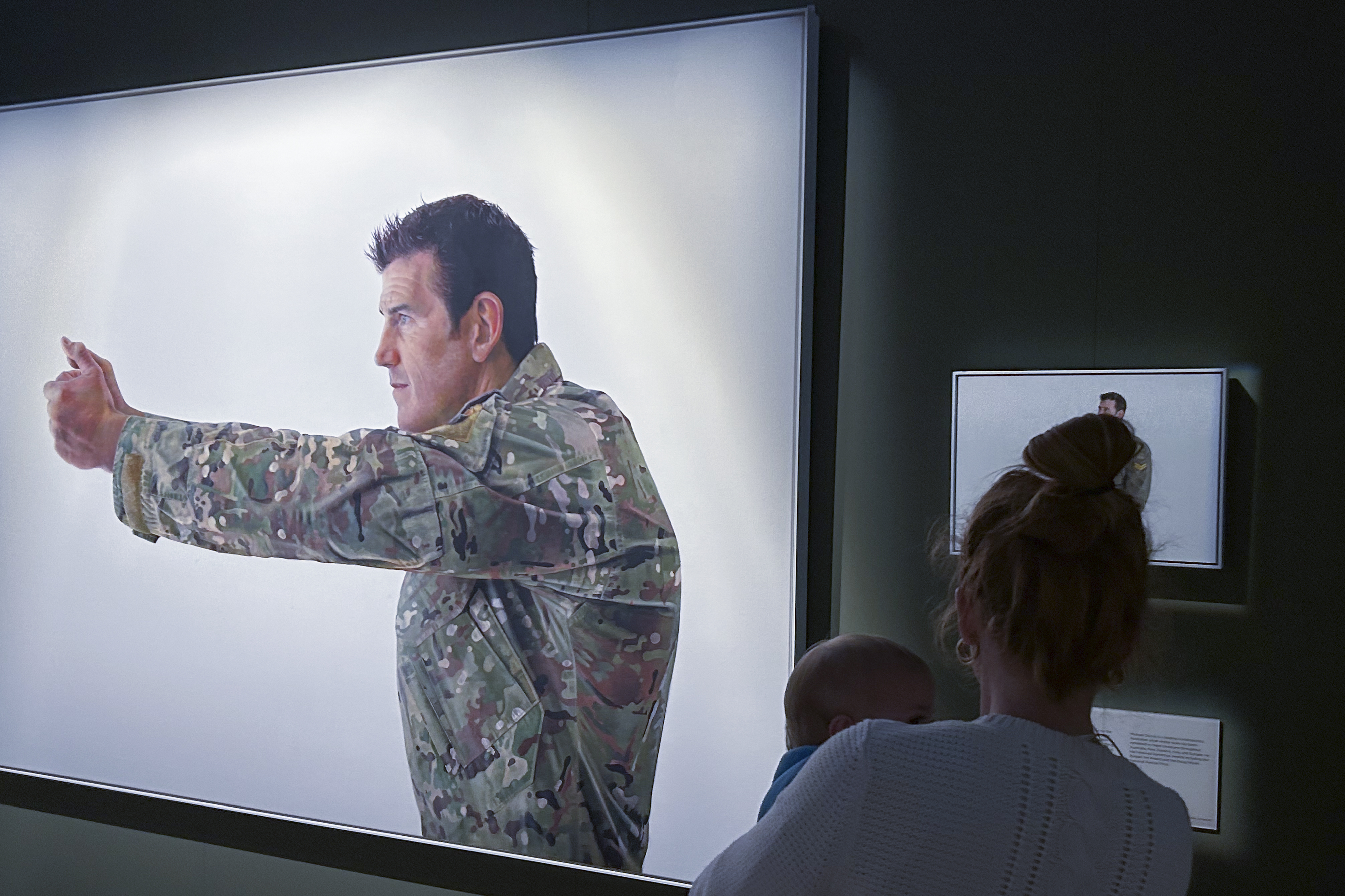 A woman looking at the portrait of Ben Roberts-Smith called Pistol Grip. He is depicted in combat uniform in a fighting stance.