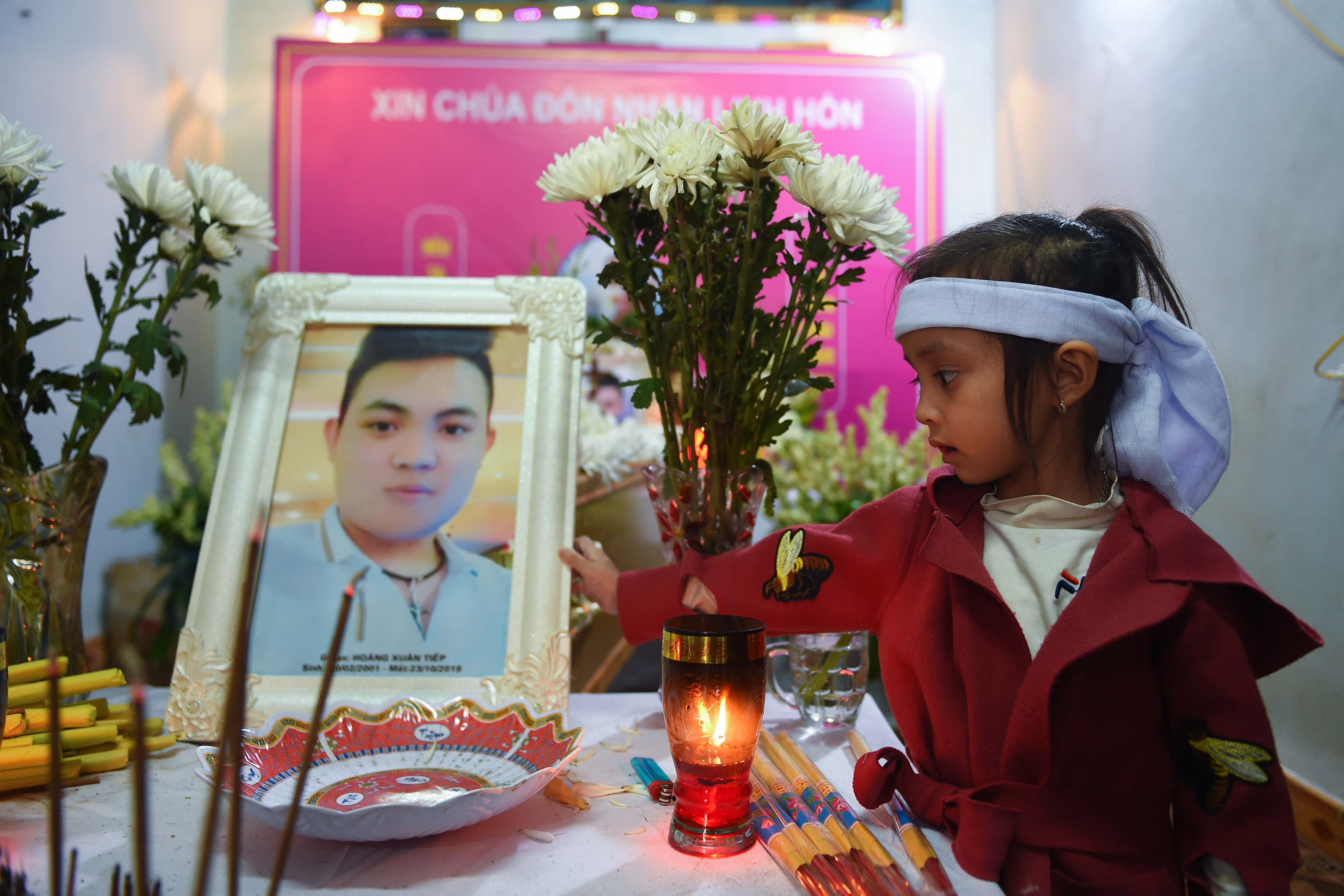 A young niece of Hoang Van Tiep holds his portrait on a coffin bearing his remains during a funeral in Dien Chau district, Nghe An province on November 28, 2019. - The families of some of the 39 Vietnamese people found dead in a truck in Britain prepared for emotional burials for their children November 28 after an agonising weeks-long wait to bring their bodies home. (Photo by Nhac NGUYEN / AFP)