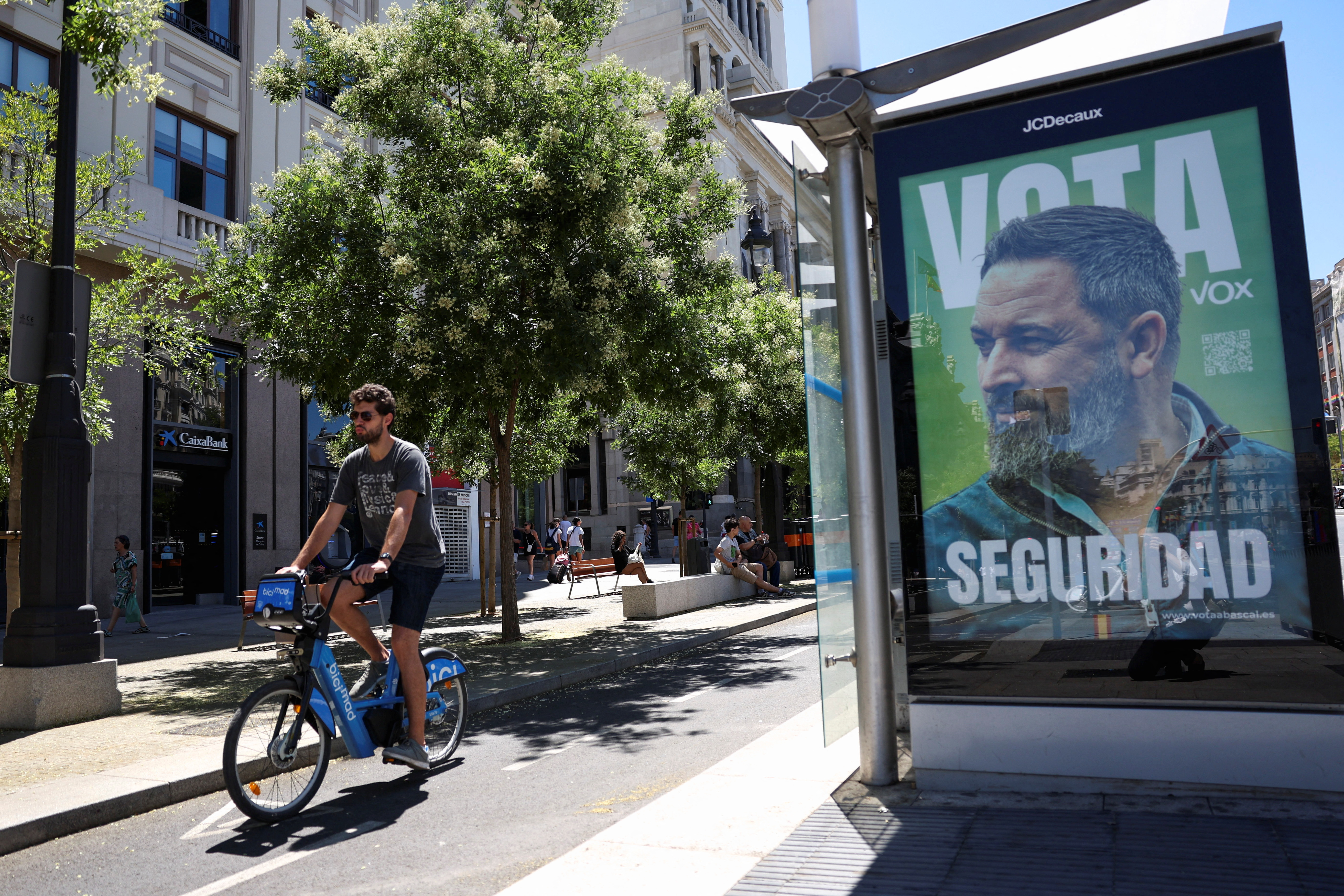 A person rides a bycicle on a bike lane past a general election campaign poster