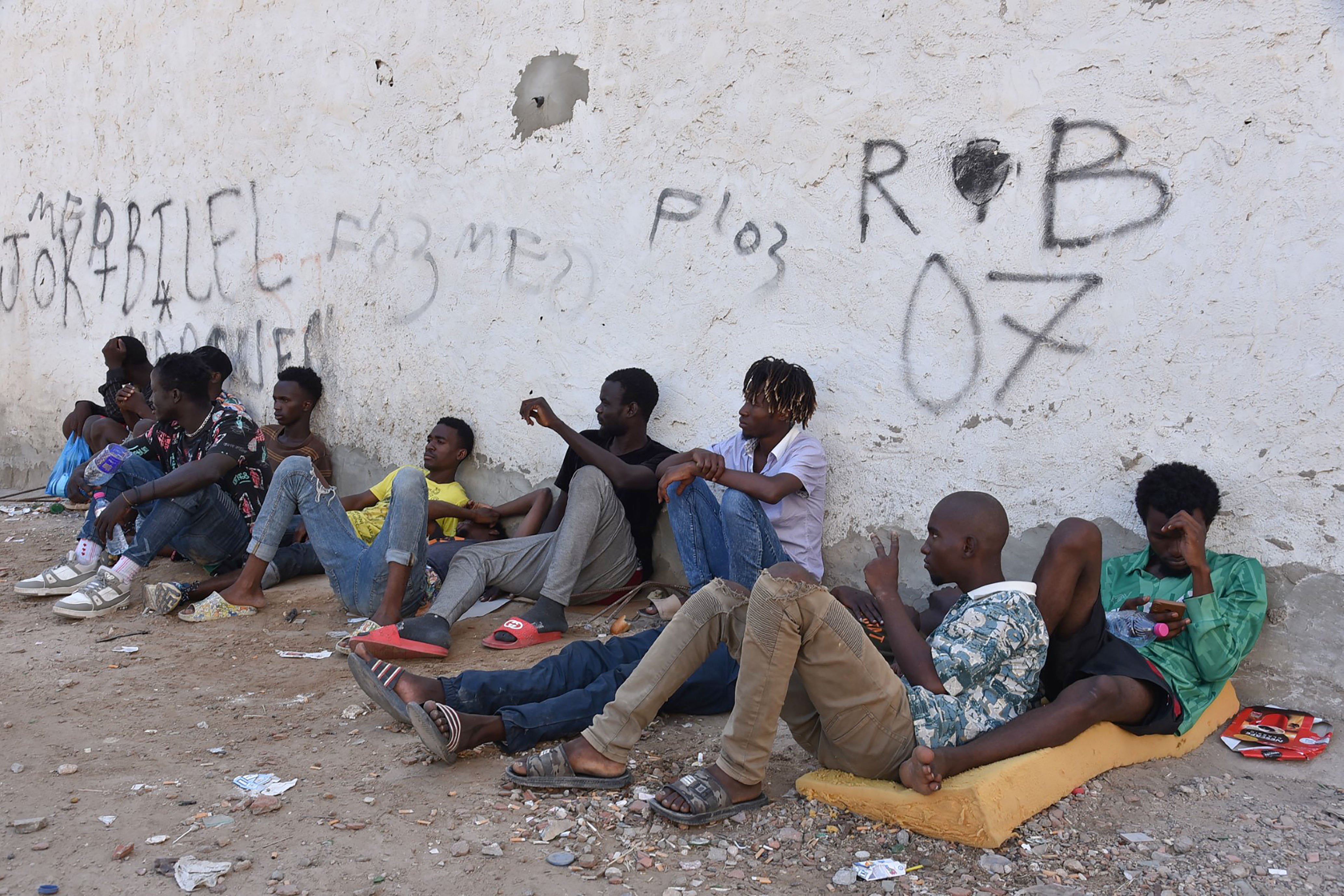 Migrants sit on the ground in Sfax as racial tensions in the Tunisian coastal city flared into violence