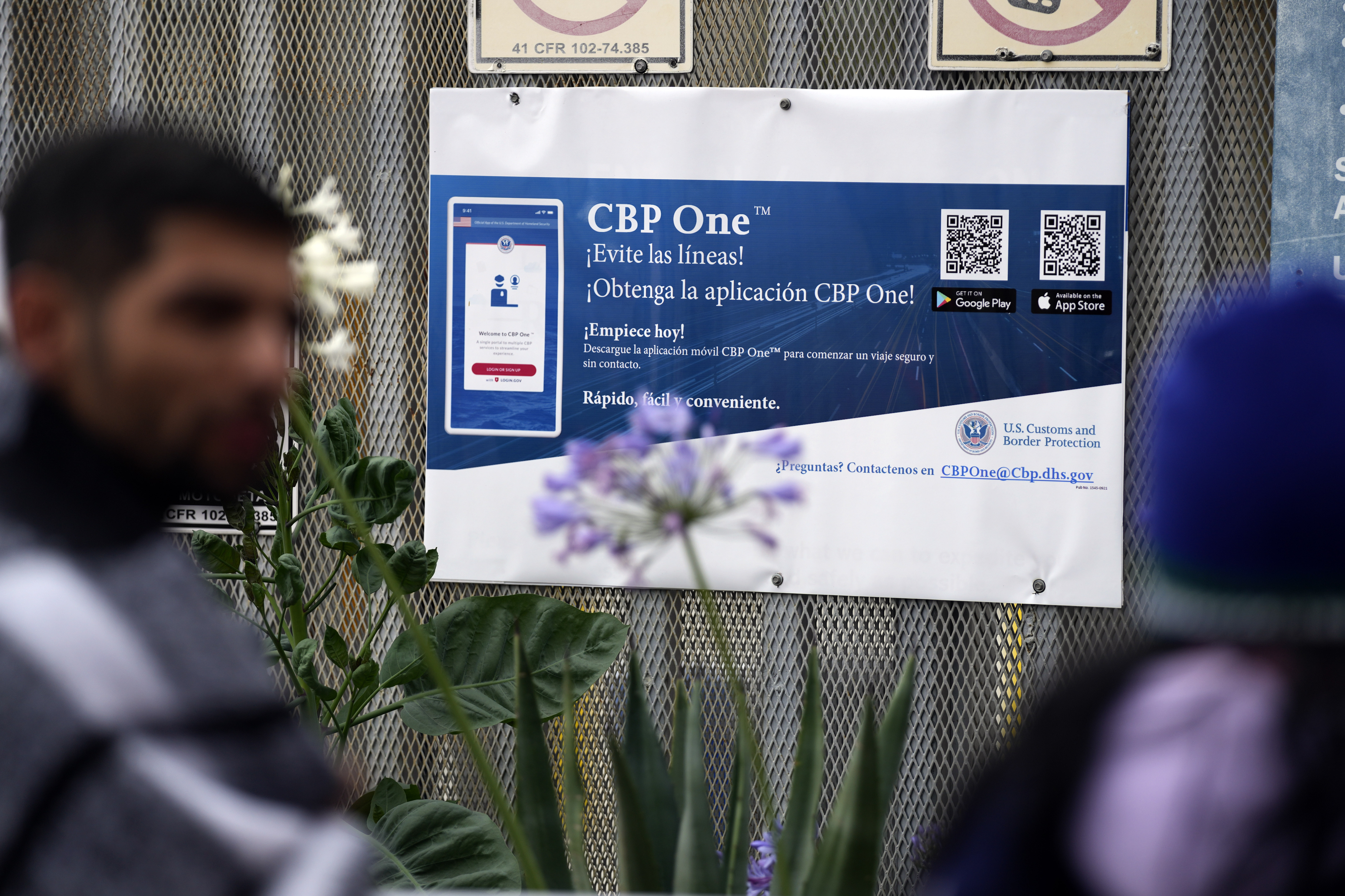 A sign advertises the CBP One mobile app as asylum seekers pass by.