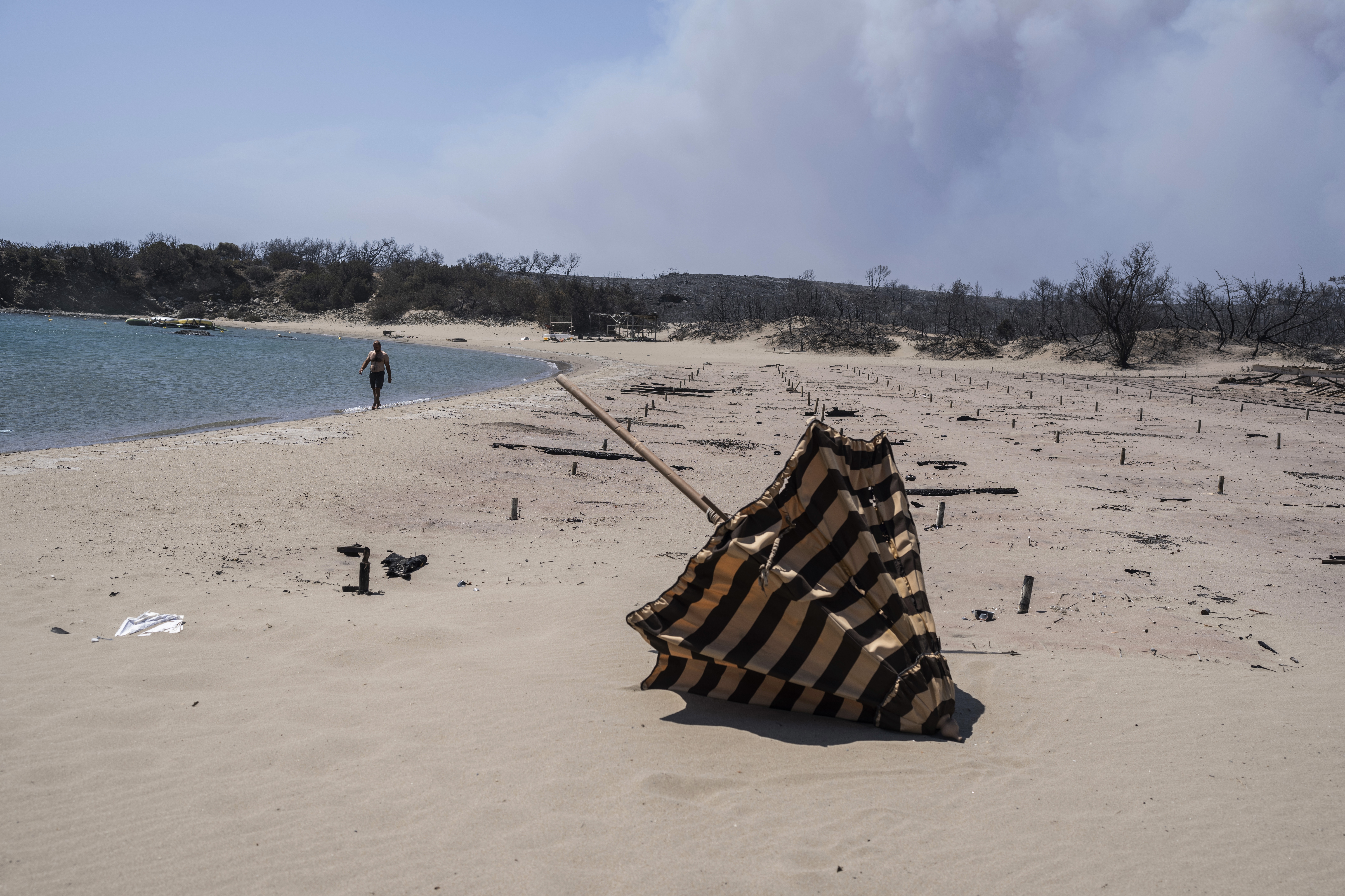 A man walks next to the burnt sunbeds and umbrellas at a beach on the Aegean Sea island of Rhodes,