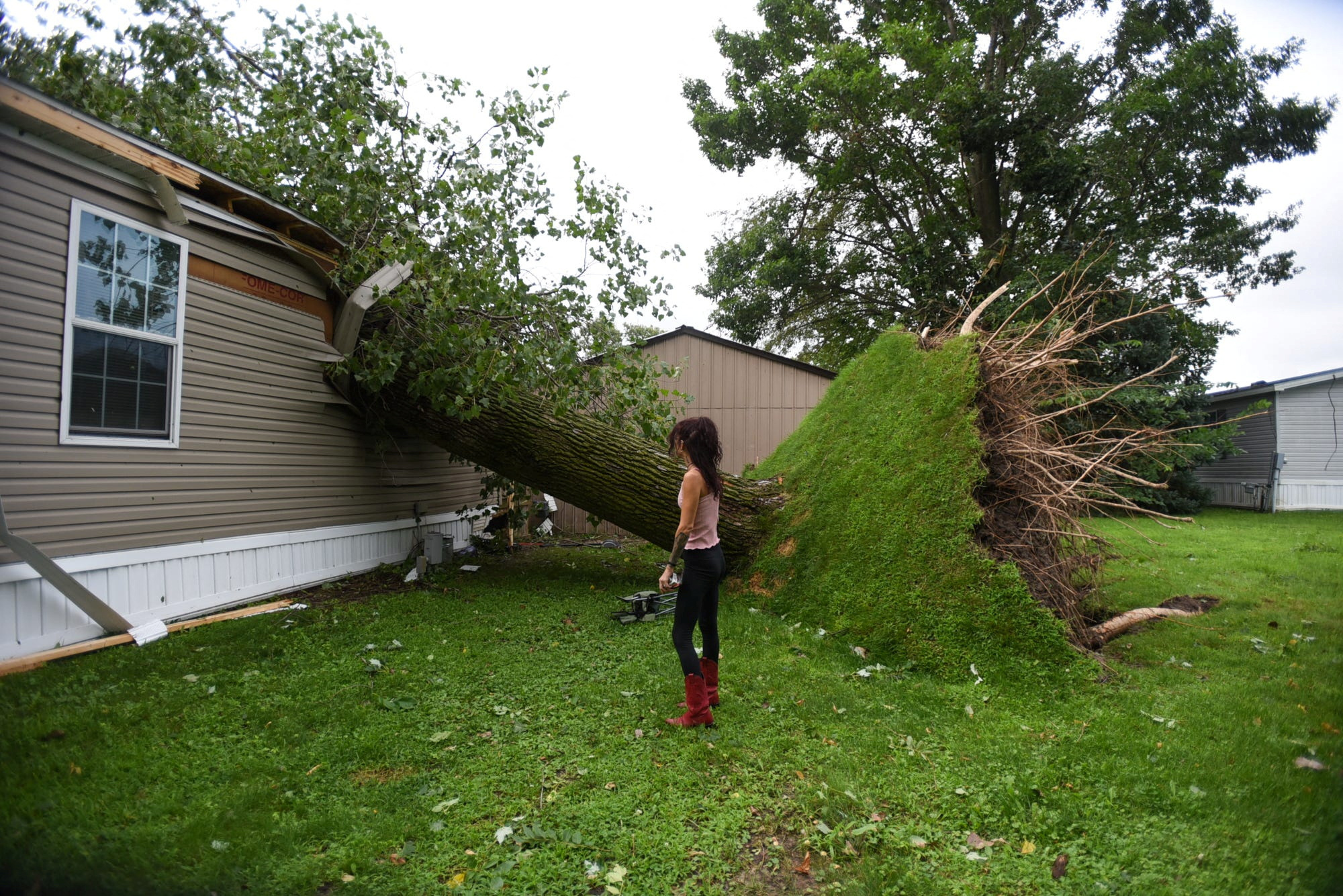 A woman looks at an uprooted tree that fell through her home after a storm.
