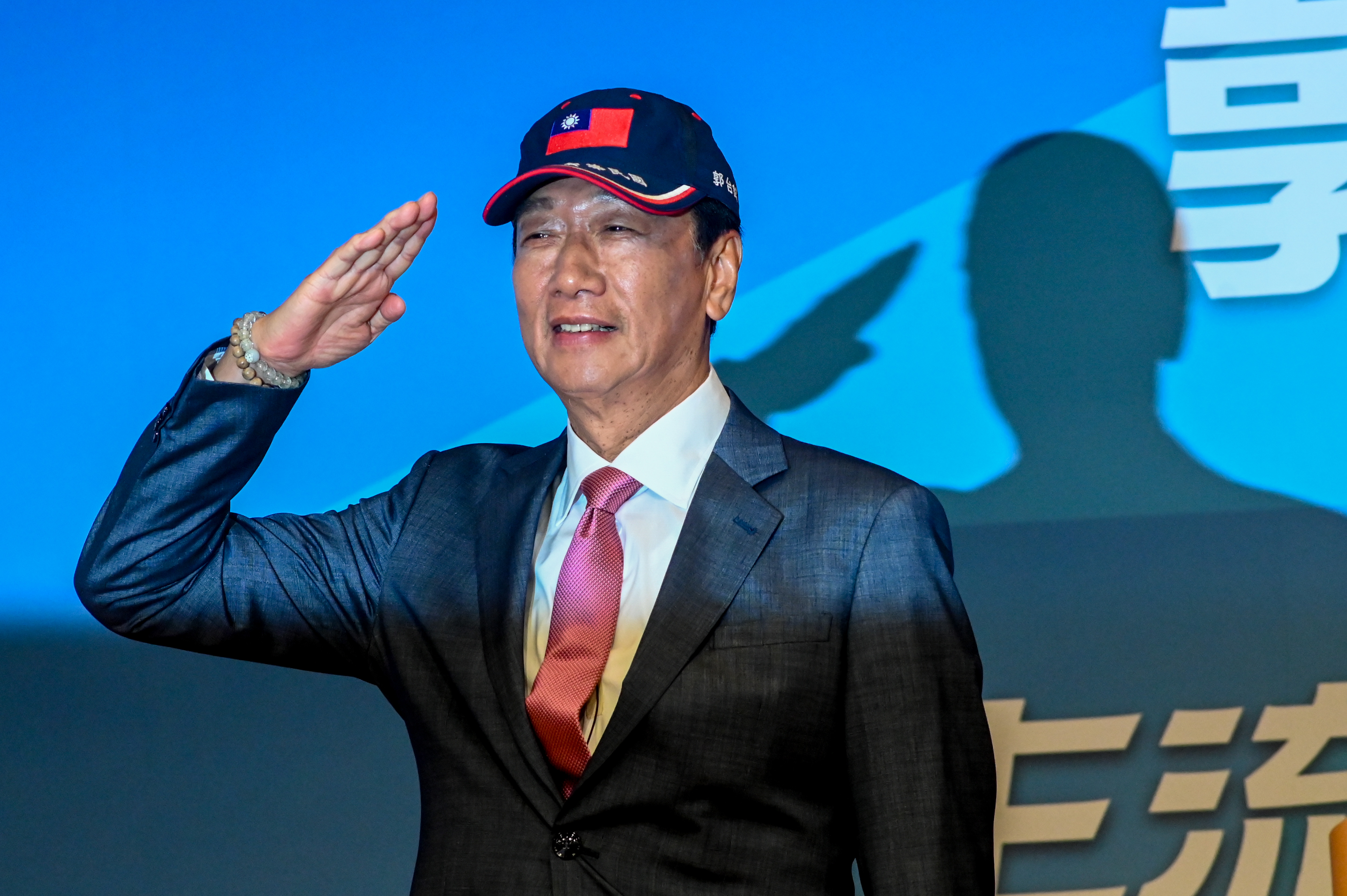 Terry Gou saluting as he announces he will run as an independent in Taiwan's presidential election. He is wearing a baseball cap with the Taiwan flag on it