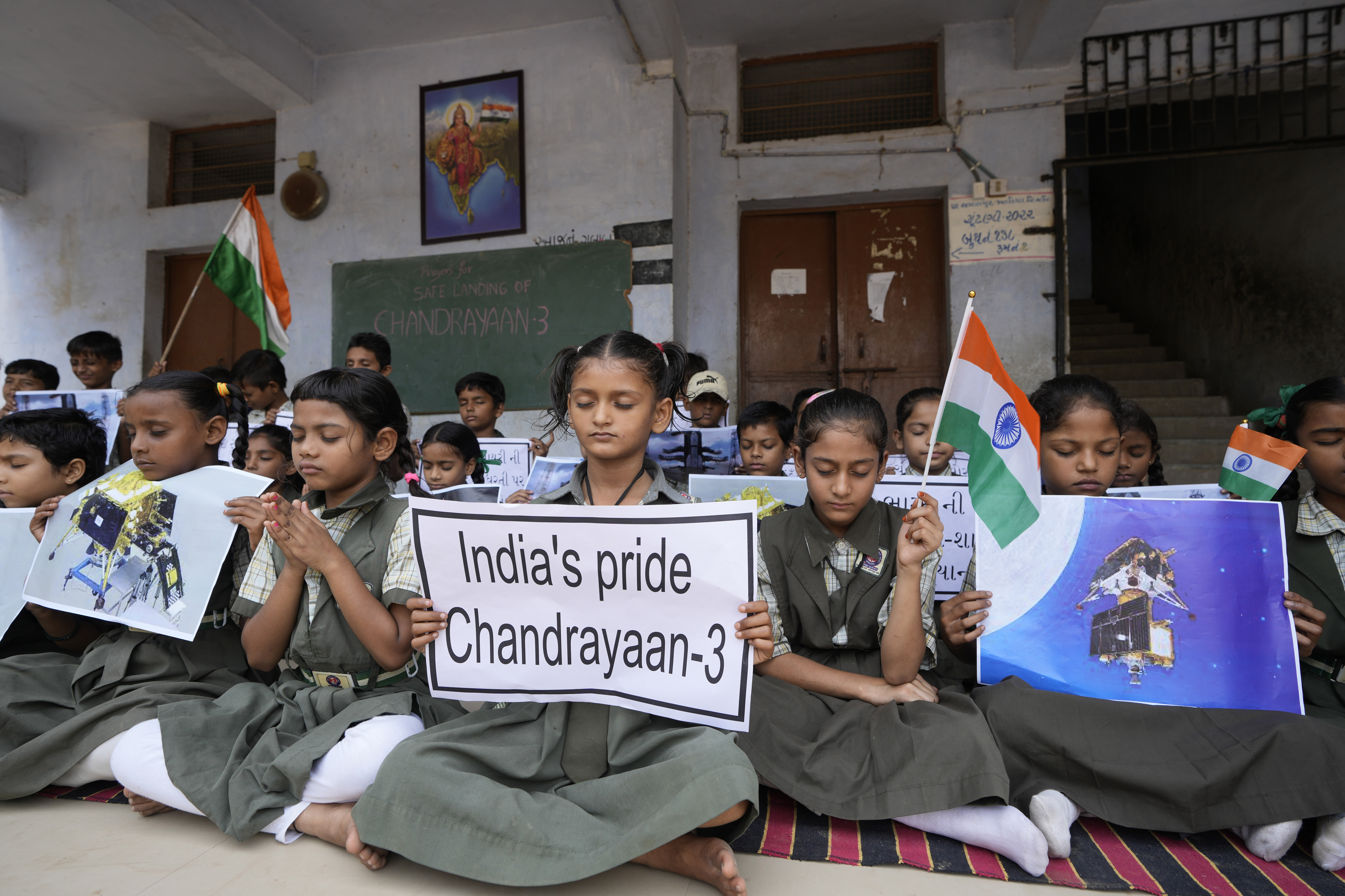 Students holds posters and pray for the successful landing of India's moon craft Chandrayaan-3, on the moon surface, at a school in Ahmedabad