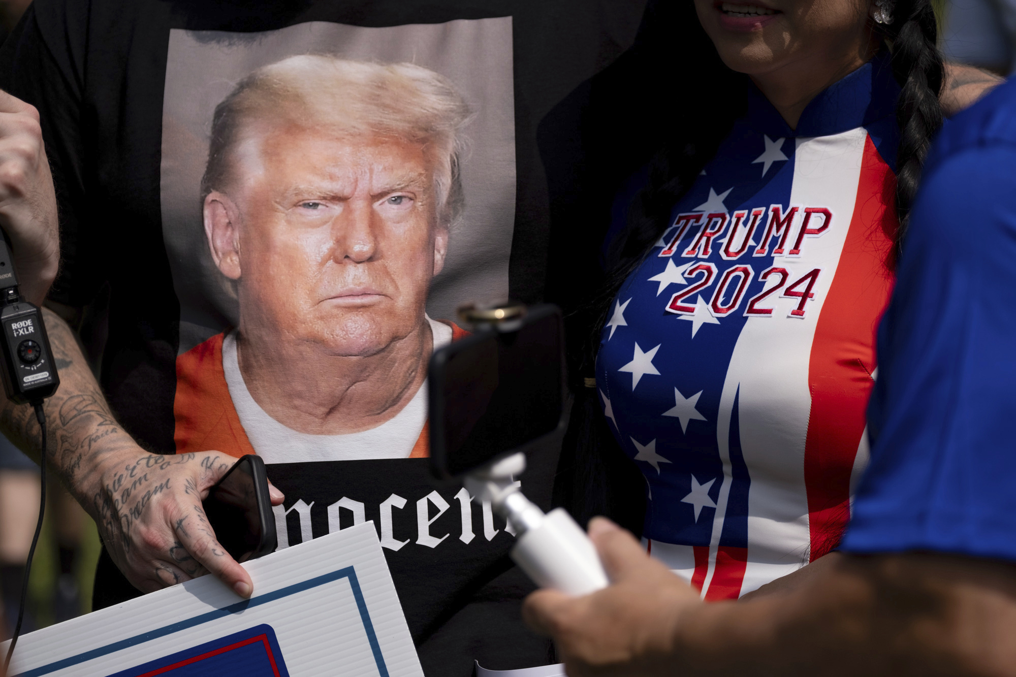 A close-up of Trump supporters wearing red-white-and-blue shirts and posters showing Trump in a prison jumpsuit.