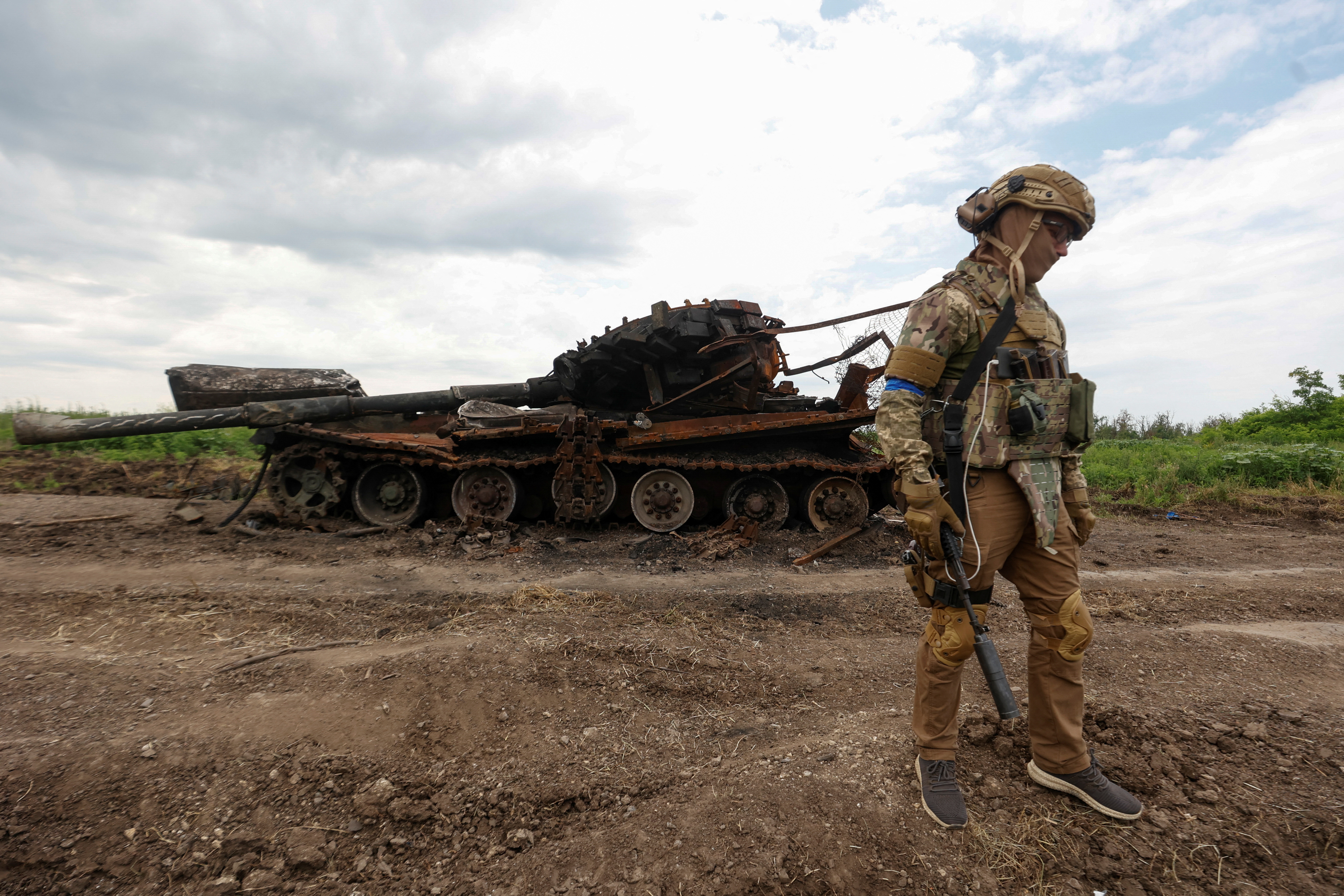 A Ukrainian serviceman stands next to a destroyed Russian tank