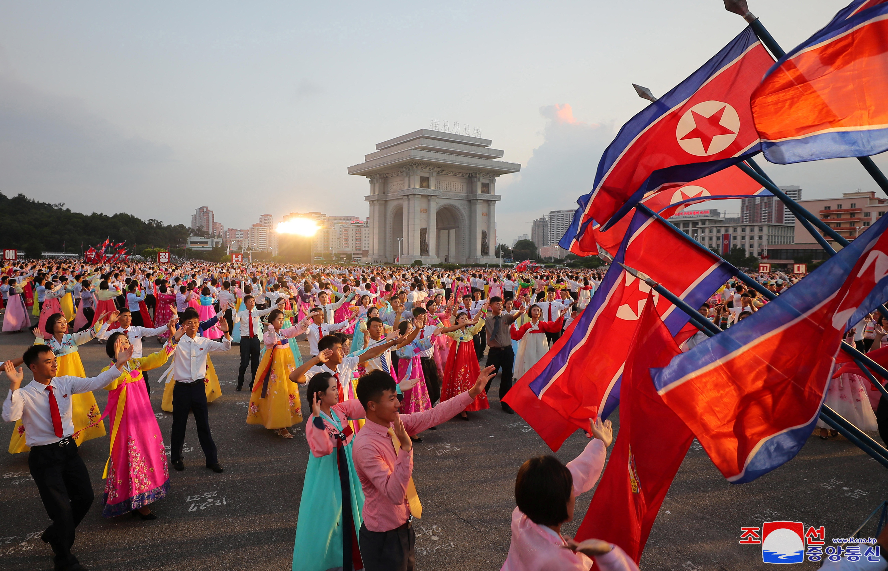 North Korean flags flying in Pyongyang at an outdoor party to mark the end of Japanese colonial rule. Many of the revellers are wearing traditional Korean clothing.