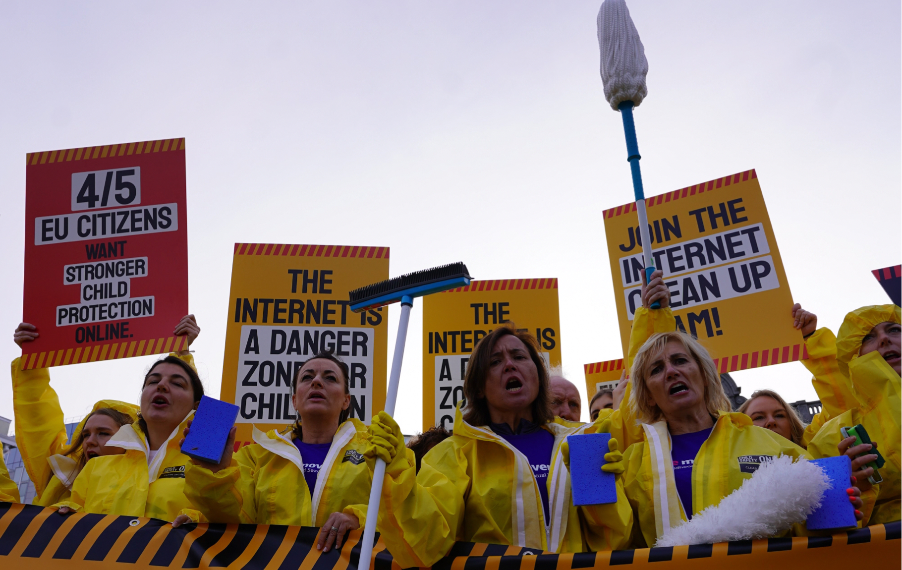 Protesters in hazmat suits holding placards and mops demand action from the EU on proliferation of childhood sexual abuse materials online