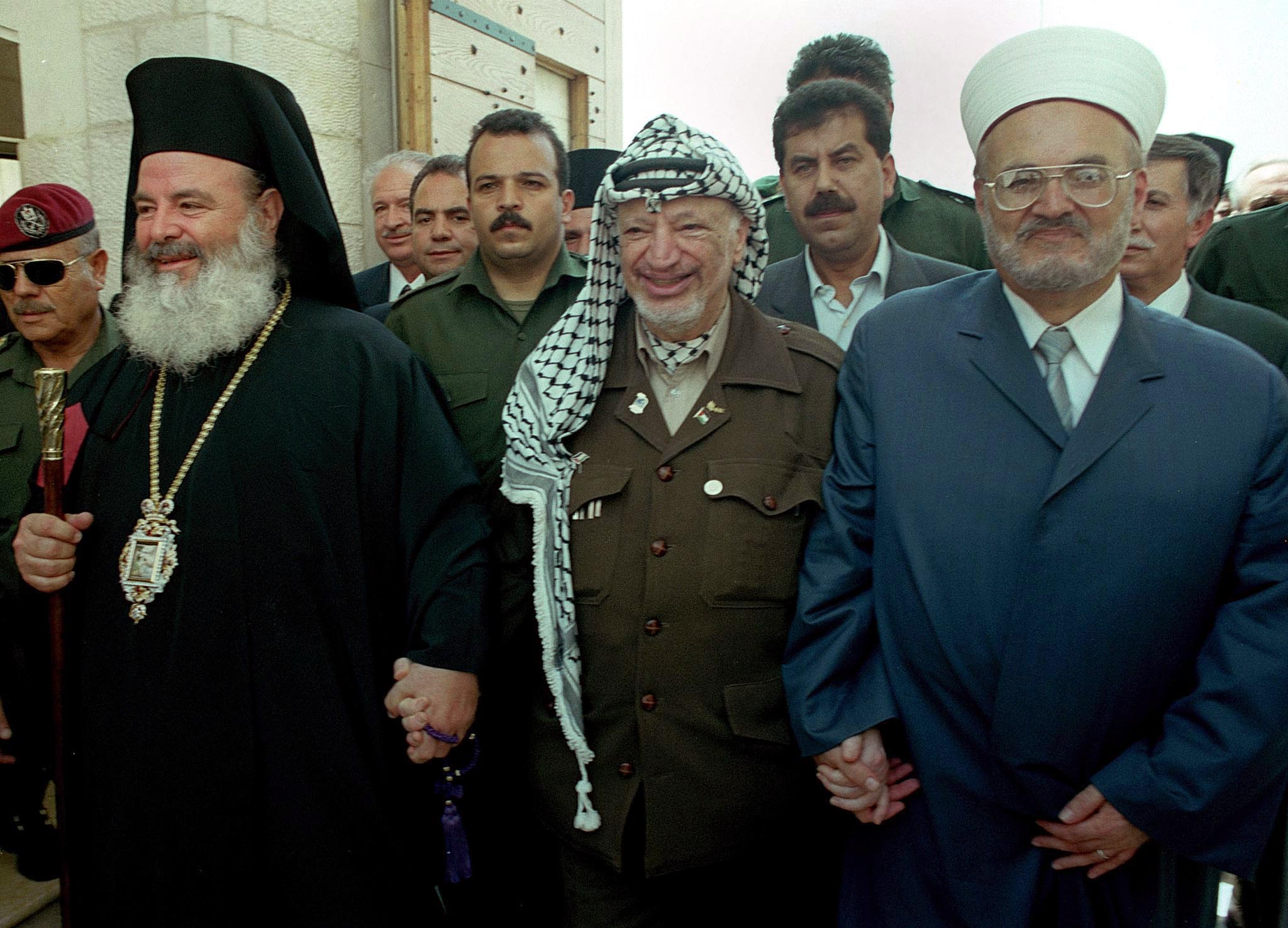 PALESTINIAN PRESIDENT YASSER ARAFAT WALKS HAND IN HAND WITH GREEK ARCHBISHOP OF ATHENS (L) AND HEAD MUSLIM CLERIC IN JERUSALEM.Palestinian President Yasser Arafat (C) walks hand in hand with Christodoulos (L), the Greek Archbishop of Athens and head of the Church of Greece, and Mufti Ikrema Sabri, the head muslim cleric in Jerusalem, prior to their meeting in Bethlehem August 25, 2000. Christodoulous will be visiting the Holy Land for a week.