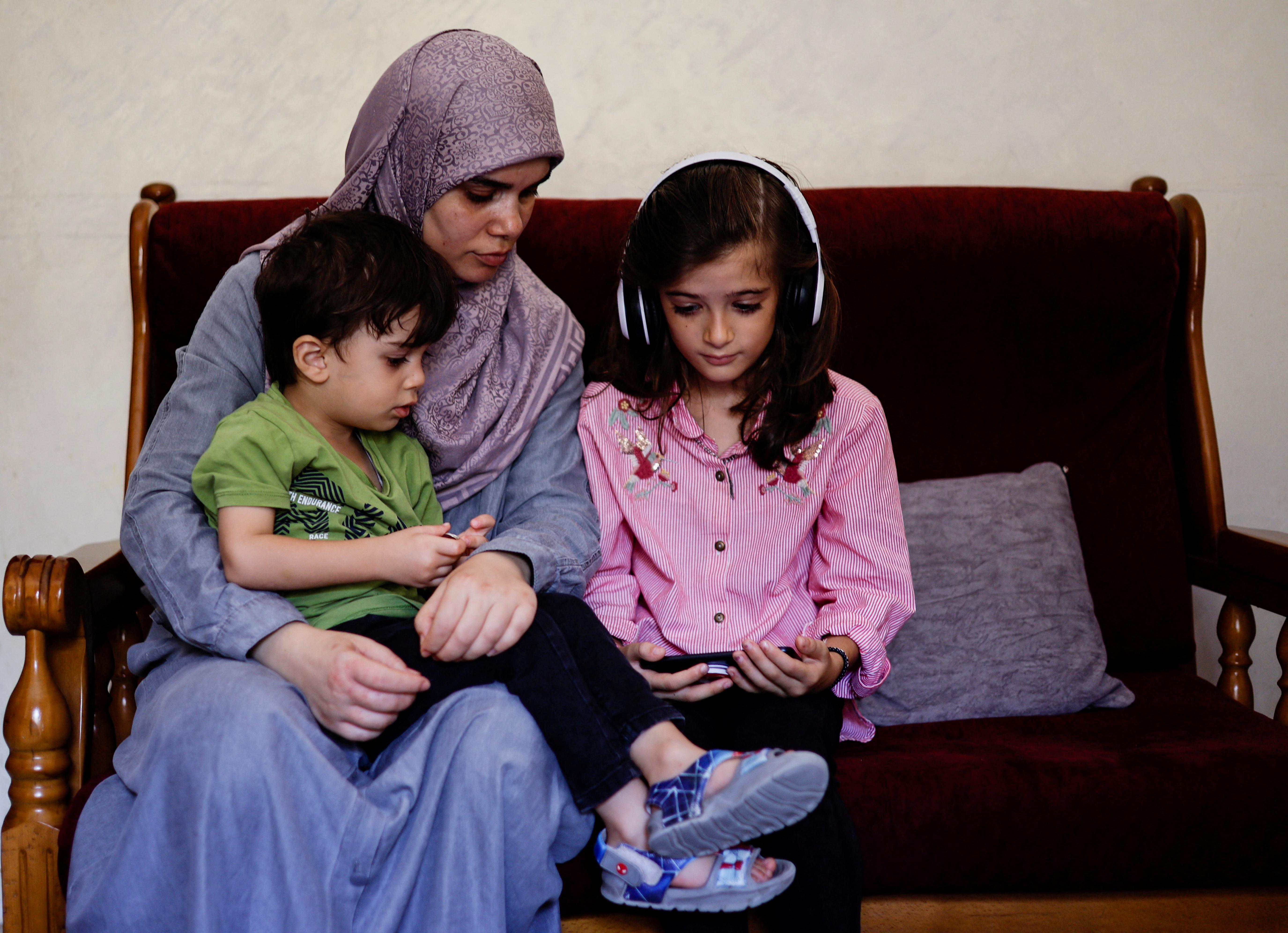 Palestinian mother Sajeda Abdu and her children Youssef and Juman look at a mobile phone