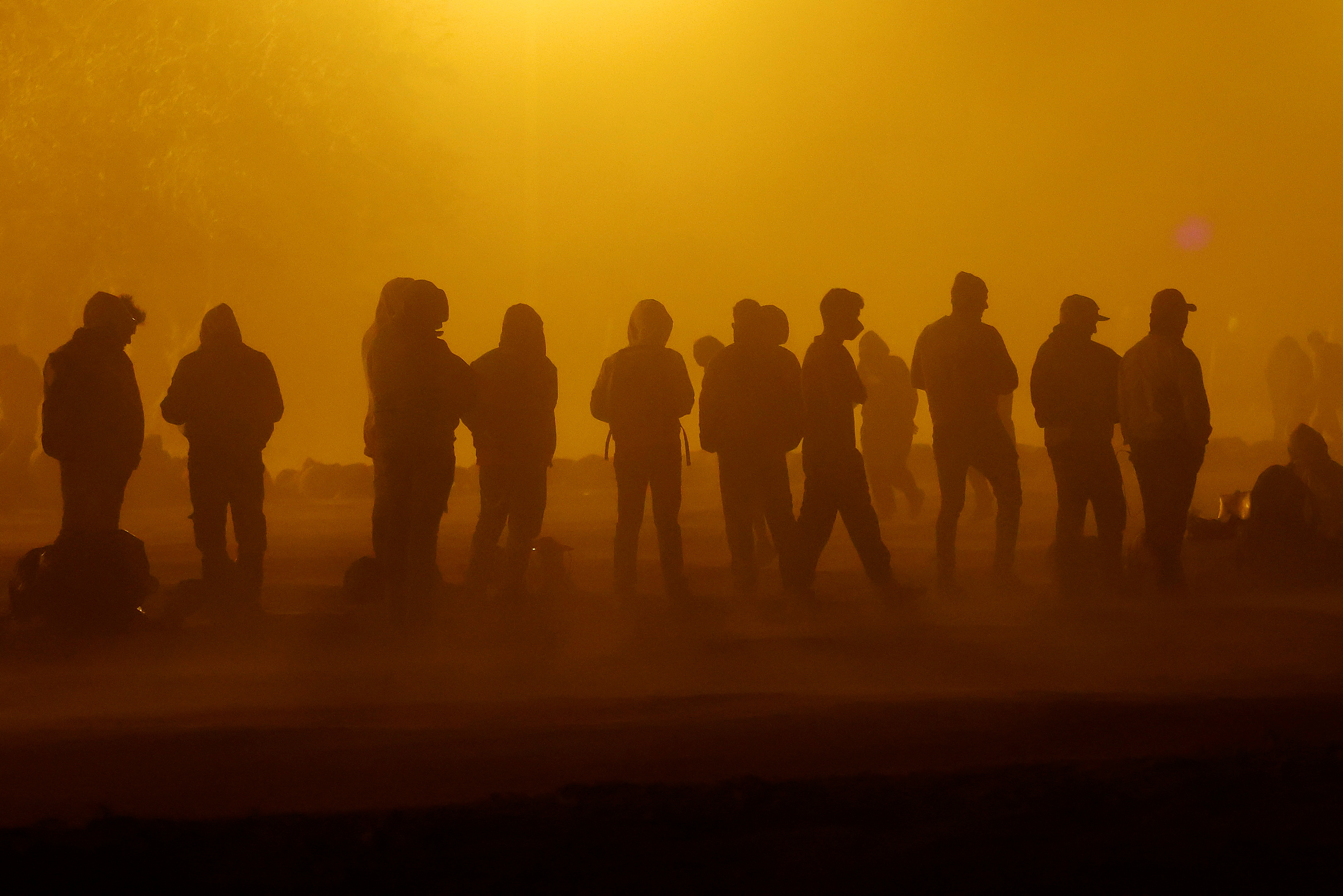 Migrants stand near the border wall during a sandstorm after having crossed the US-Mexico border to turn themselves in to US Border Patrol agents [File: Jose Luis Gonzalez/Reuters] 