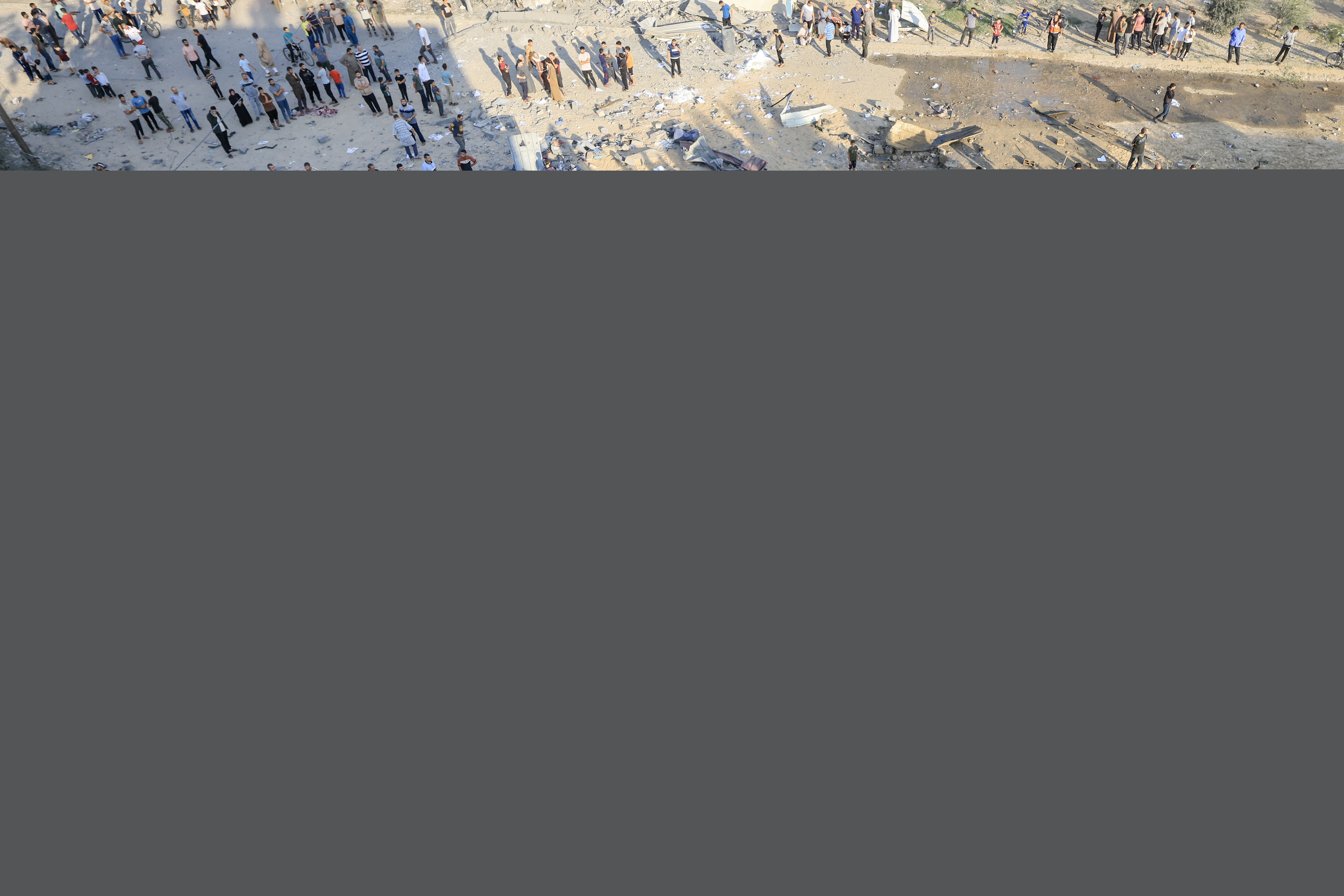 Palestinians stand next to a crater caused by an explosion from an Israeli airstrike